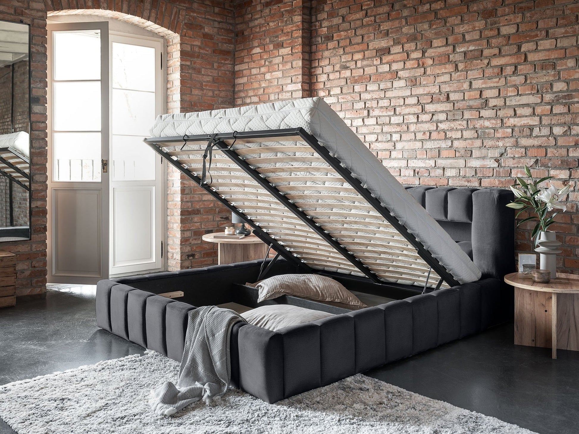 Widok schowka od boku: Otwarty stelaż łóżka Monolith 85 szary 140×200 cm, eksponujący pojemny, czarny schowek na pościel.