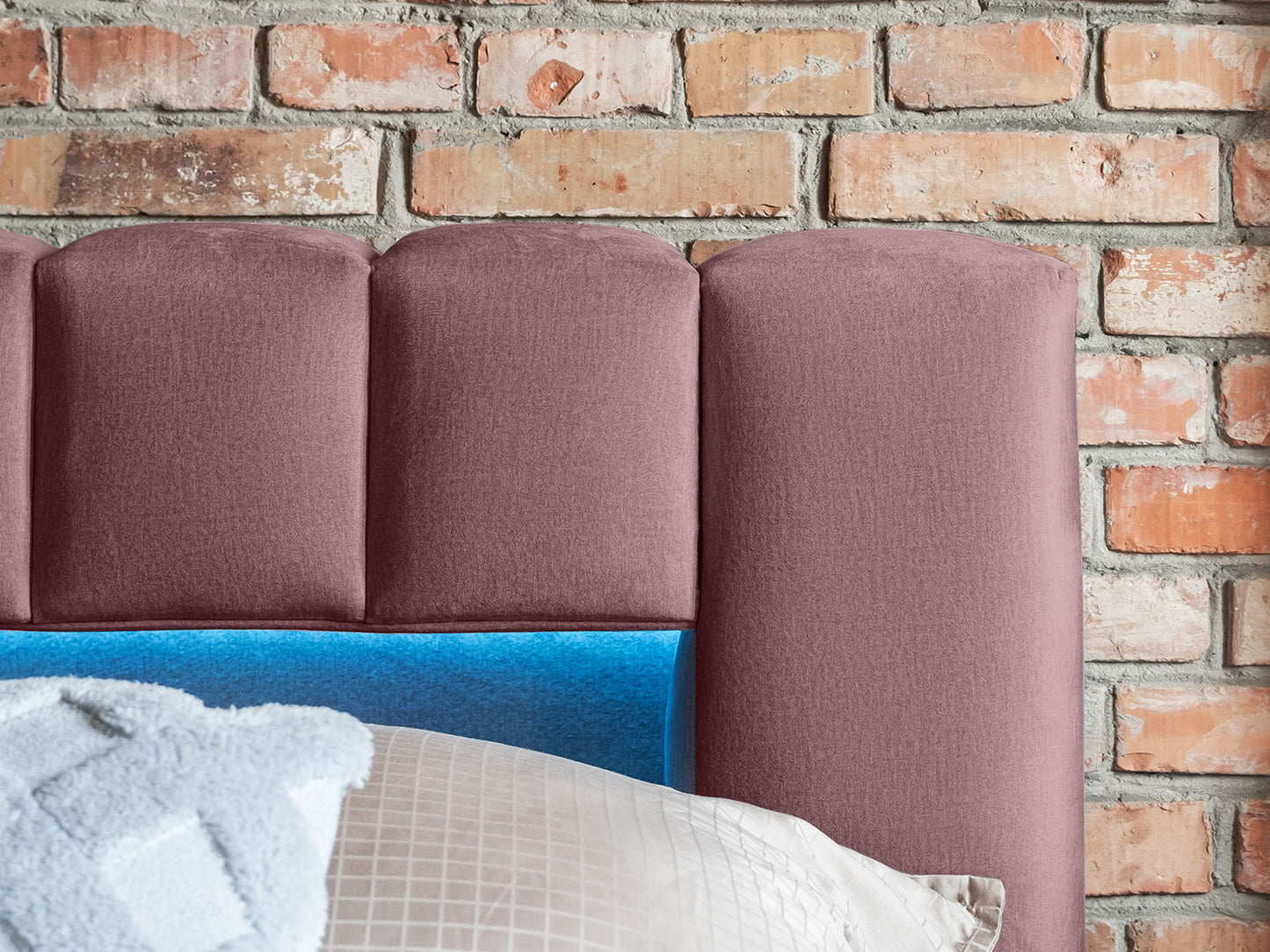 Zbliżenie na pikowany zagłówek łóżka Lamica II Monolith 63 różowy z wbudowanym oświetleniem LED na tle ceglanej ściany.