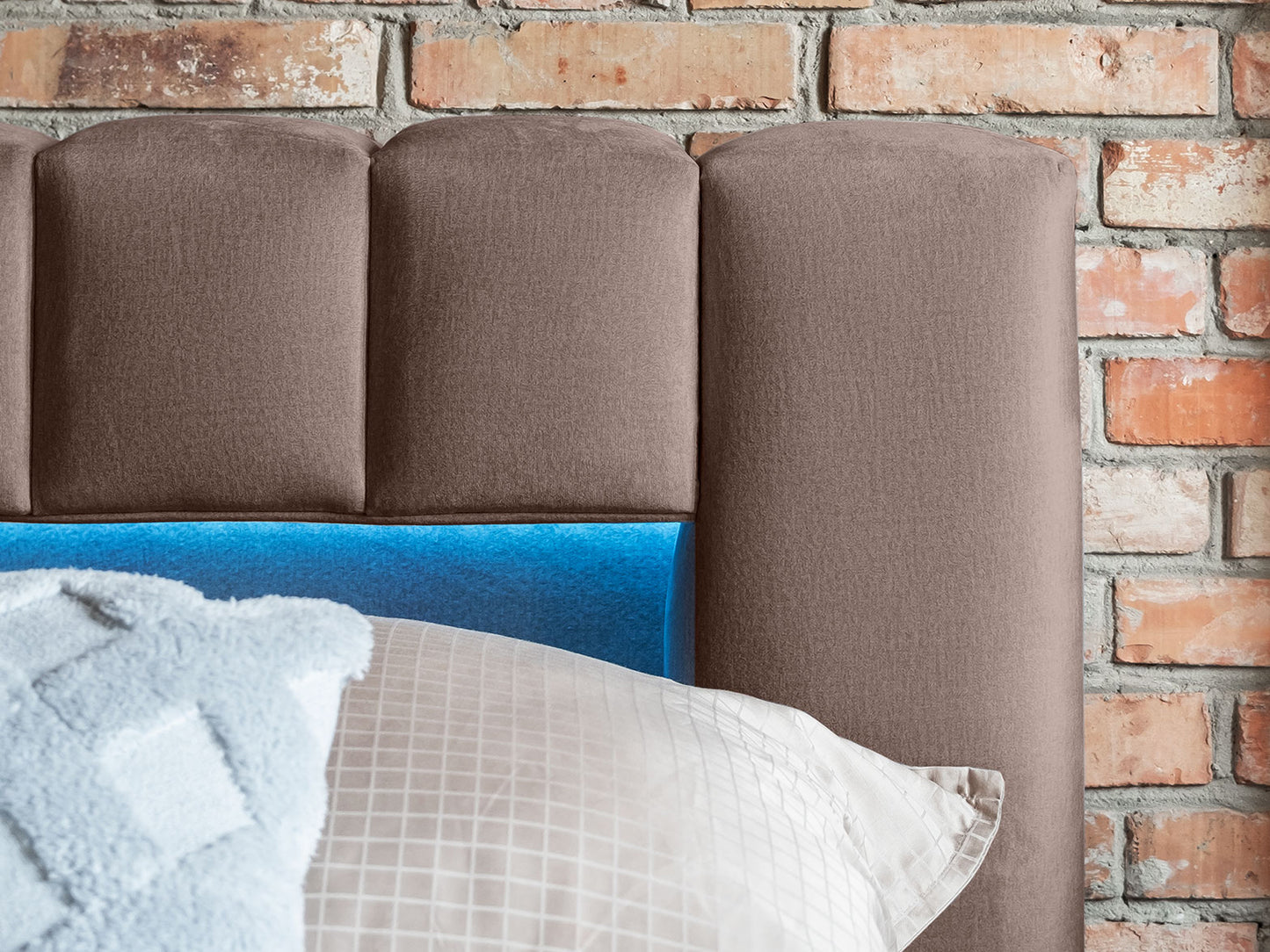 Zbliżenie na wezgłowie łóżka Lamica II Monolith 09 piaskowy z niebieskim podświetleniem LED na tle ceglanej ściany.