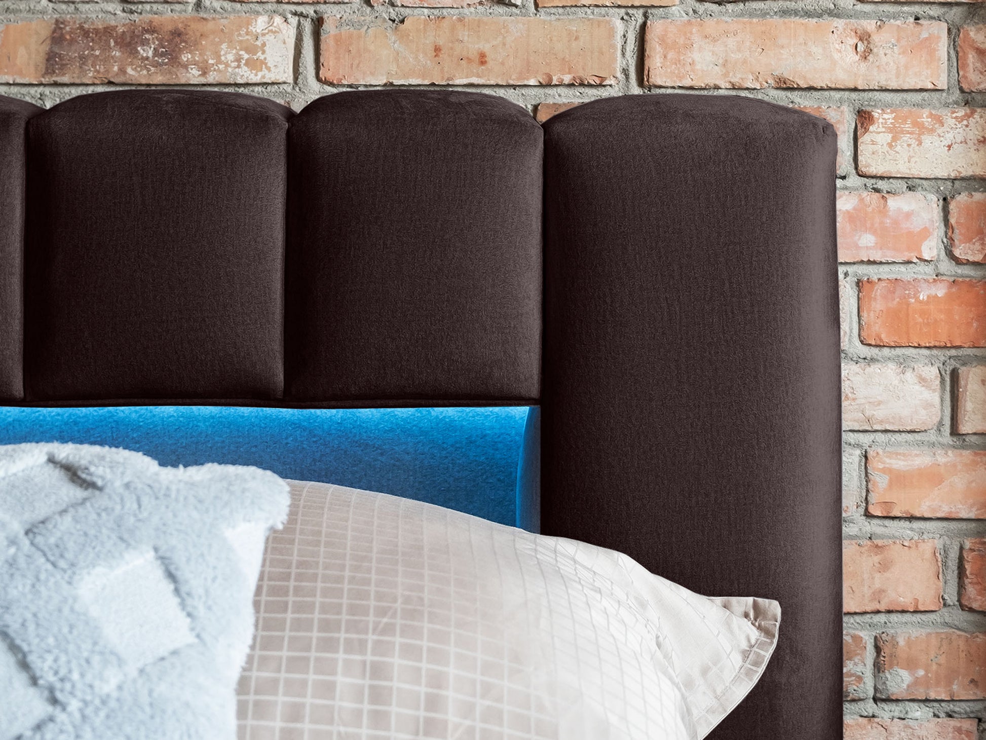 Zbliżenie na górną część zagłówka łóżka Lamica II Monolith 29 brązowy na tle ceglanej ściany, z niebieskim światłem LED.