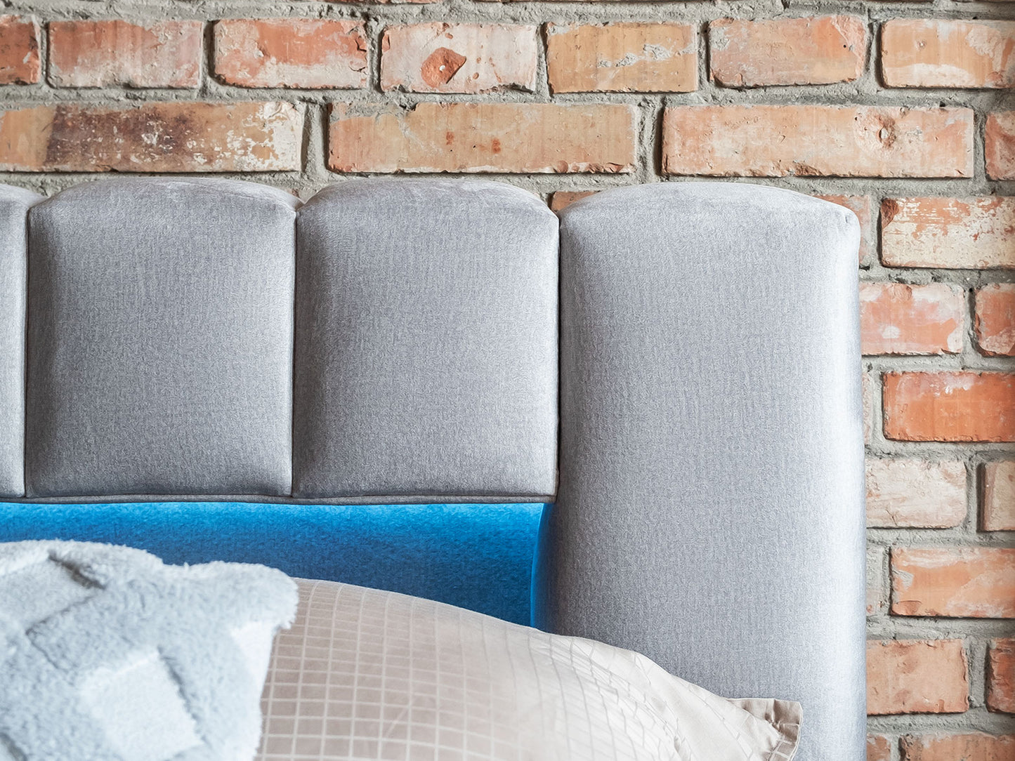 Zbliżenie na zagłówek łóżka Lamica II w tkaninie Monolith 84 jasnoszary z podświetleniem LED, na tle ceglanej ściany.