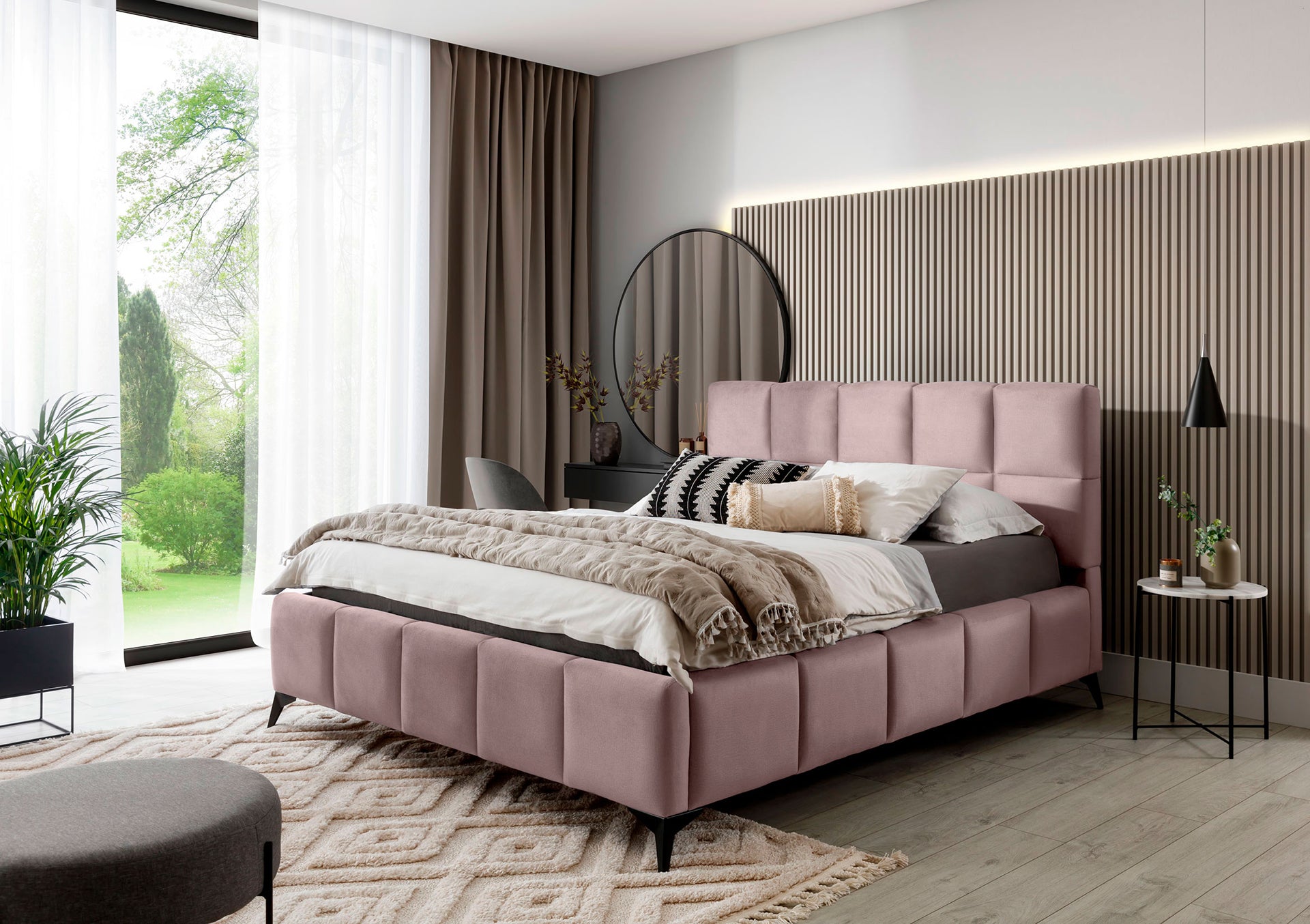Łóżko Mist w odcieniu Loco 24 jasnoróżowy 180x200 cm ustawione w nowoczesnej sypialni z dużym oknem i eleganckimi dodatkami.