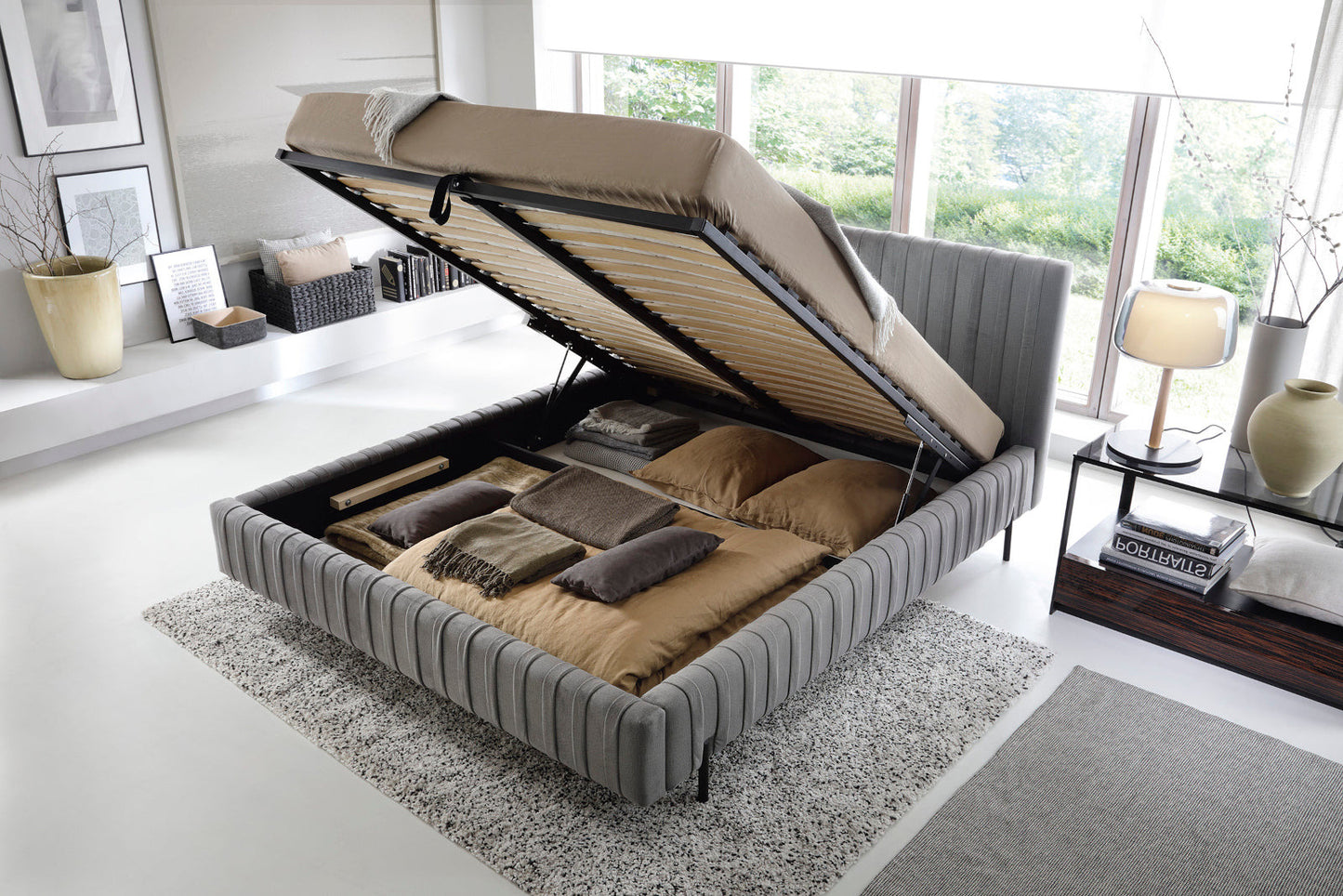 Łóżko Plissa 140×200 w obiciu Nube 05 ciemnoszarym z podnoszonym stelażem odsłaniającym pojemny schowek na pościel, ustawione na jasnoszarym dywanie.