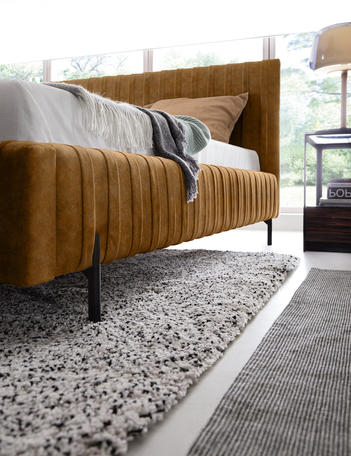 Niski kąt patrzenia na bok i czarną nogę łóżka Plissa 180×200 w kolorze Relax 45 żółty, umieszczone na teksturowanym jasnym dywanie.