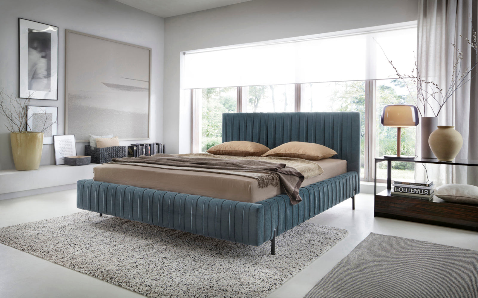 Nowoczesne łóżko Plissa w kolorze Velvetmat 100 jasnoniebieskim w jasnej sypialni z dużym oknem i beżową pościelą.