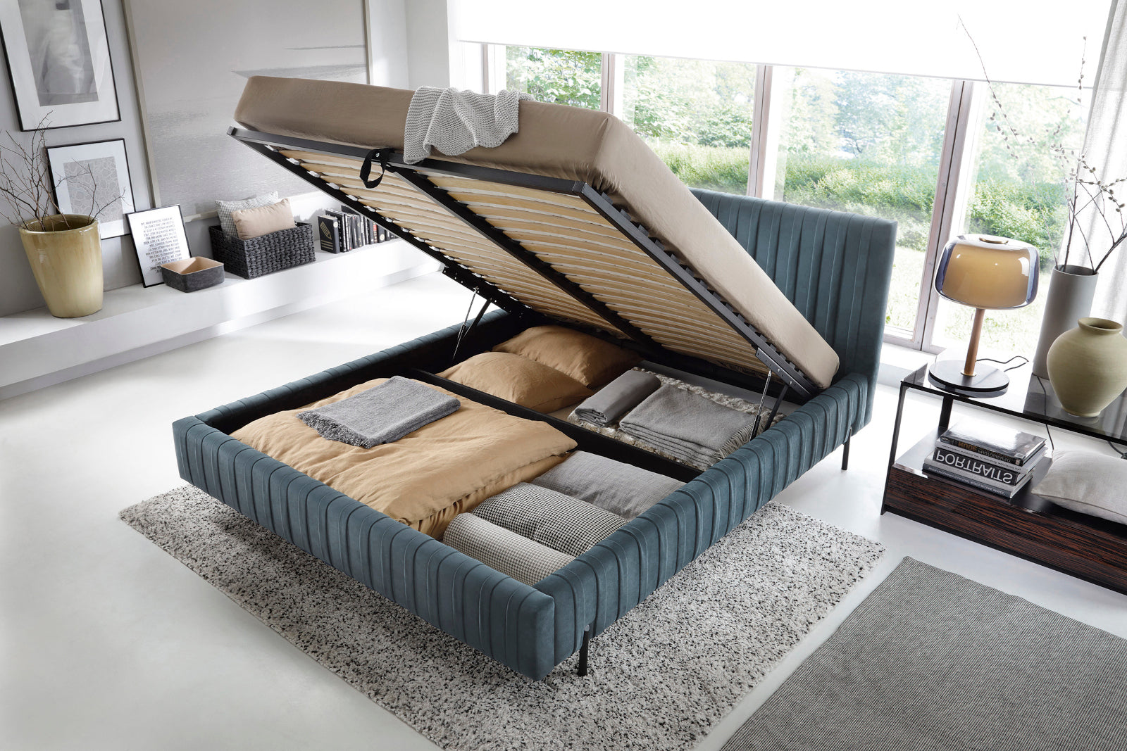 Łóżko Plissa 180×200 w welwetu Velvetmat 100 jasnoniebieskim z podnoszonym stelażem odsłaniającym pojemny schowek na pościel, ustawione na jasno szarym dywanie.