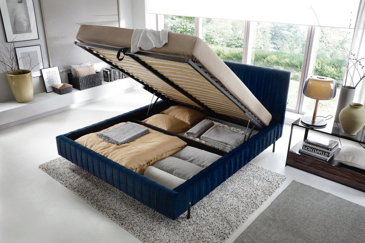 Podniesiony stelaż łóżka Plissa 180×200 Velvetmat 40 granatowy odsłaniający przestronny schowek na pościel tapicerowany welurem.