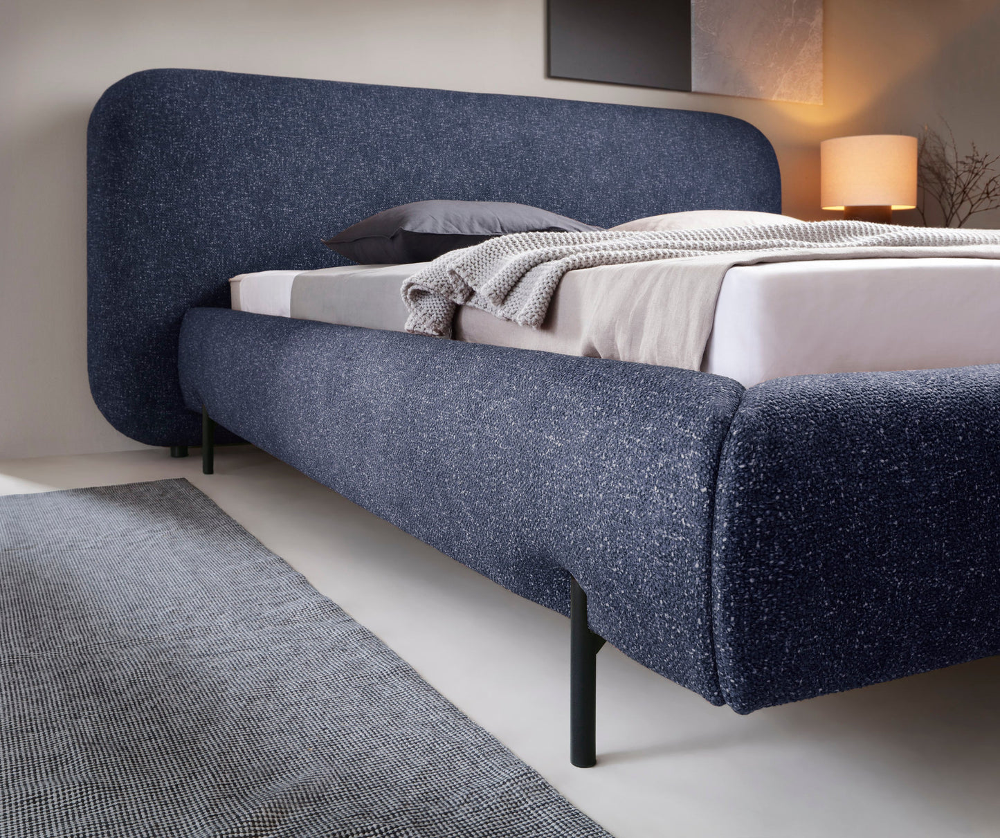 Zbliżenie na korpus łóżka Pointt w tkaninie Breona 40 niebieskiej, z widoczną nogą, materacem i pościelą w aranżacji sypialni.