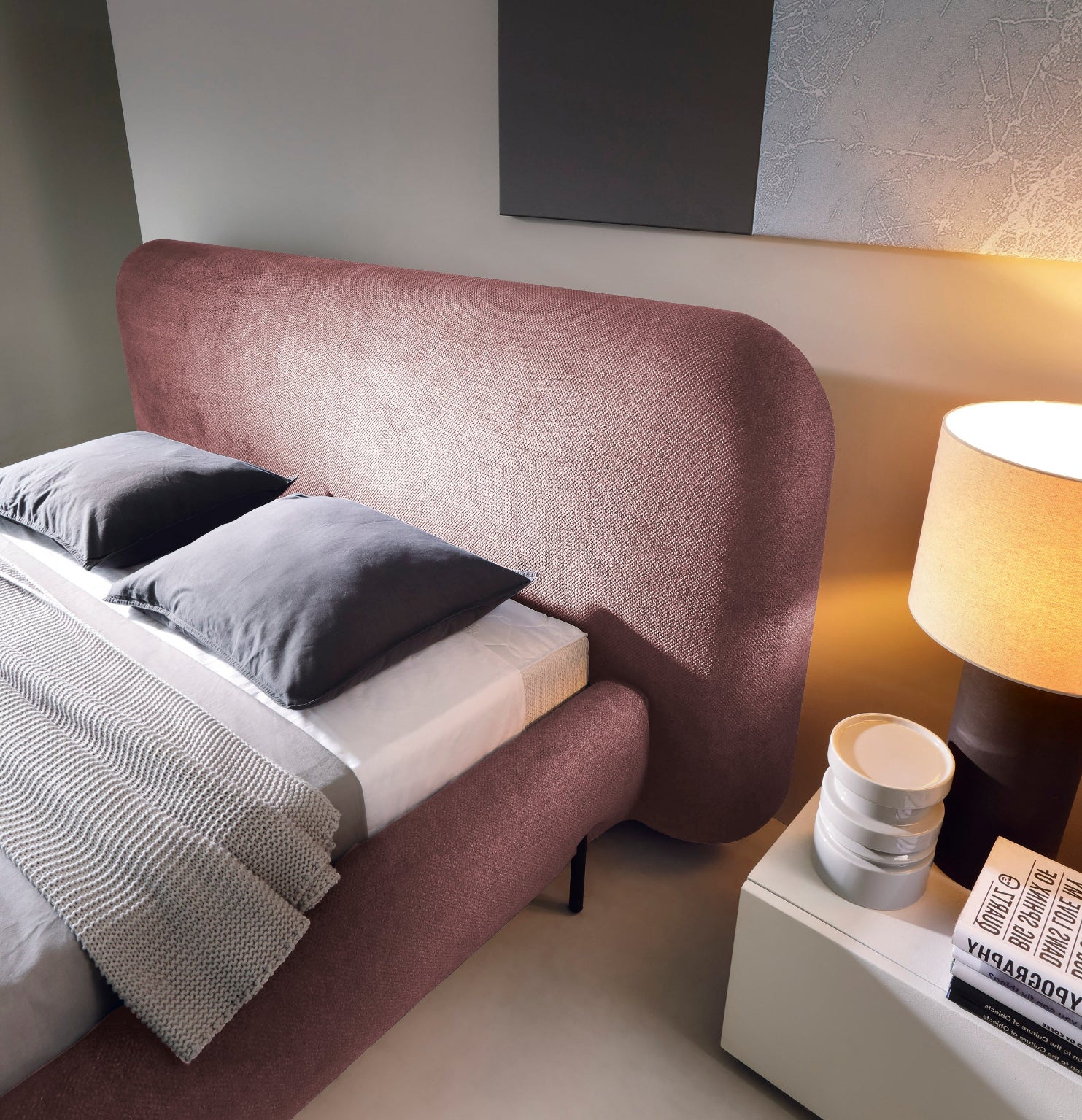 Zbliżenie na zagłówek łóżka Pointt Paolli 24 w kolorze różowym – tapicerowany panel o zaokrąglonych krawędziach w aranżacji sypialni z lampką nocną.