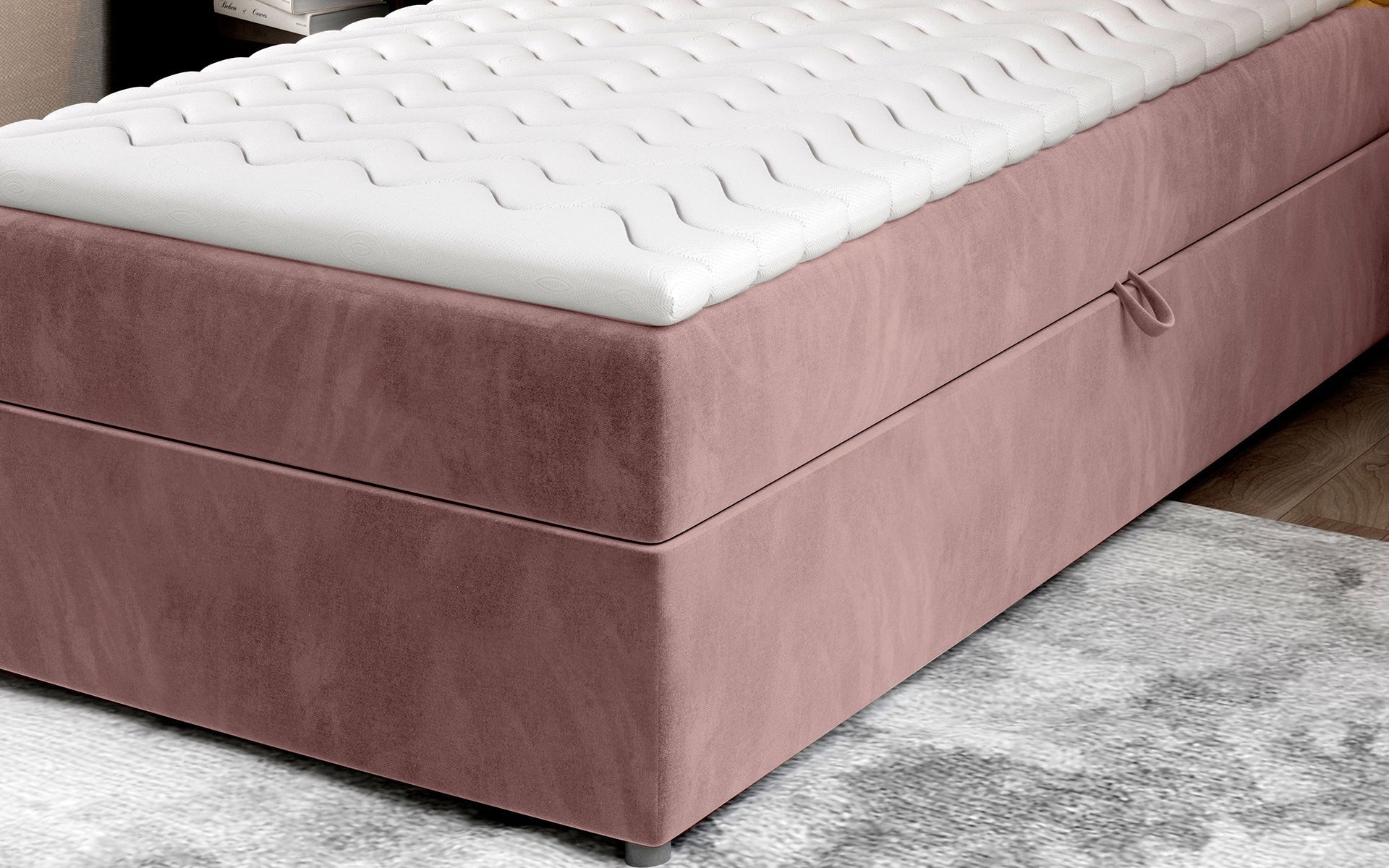 Zbliżenie na dolną część łóżka Rivia w kolorze Monolith 63 różowy o wymiarach 90x200 cm, z widocznym pojemnikiem na pościel.