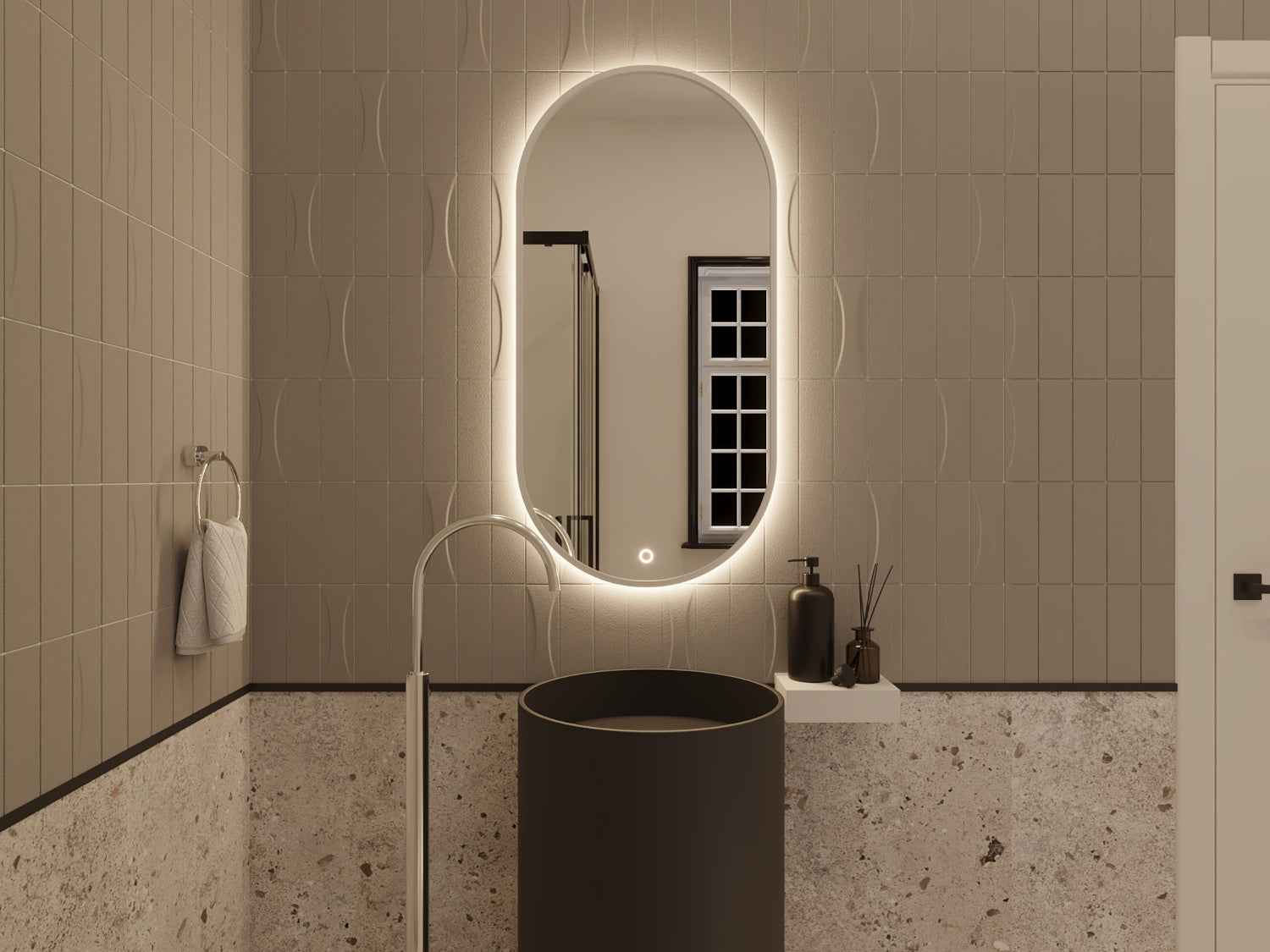 Białe owalne lustro Arducati A 50×100 cm z ciepłym LED-owym podświetleniem zamontowane na beżowo-szarej ścianie nad czarną, okrągłą umywalką.