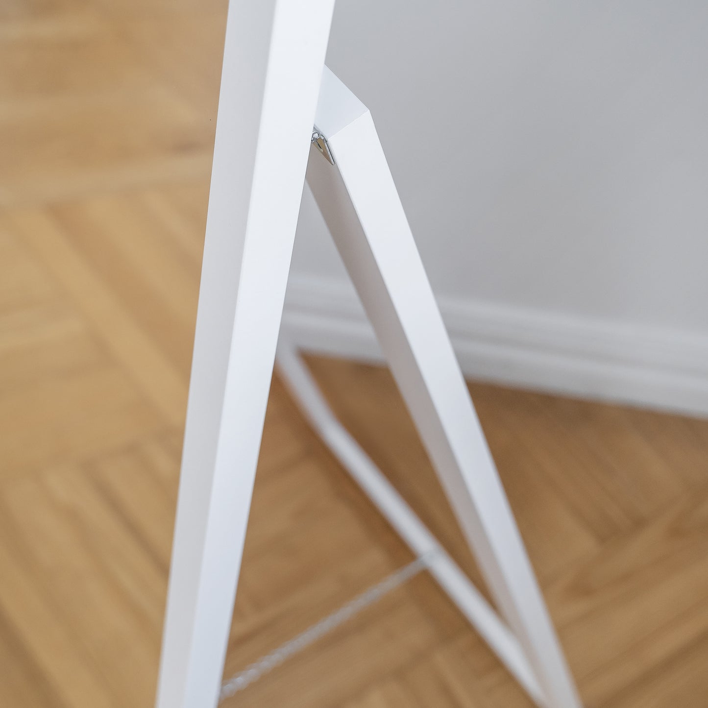 Dolna część stojaka lustra Verona w białej ramie na tle drewnianej podłogi.