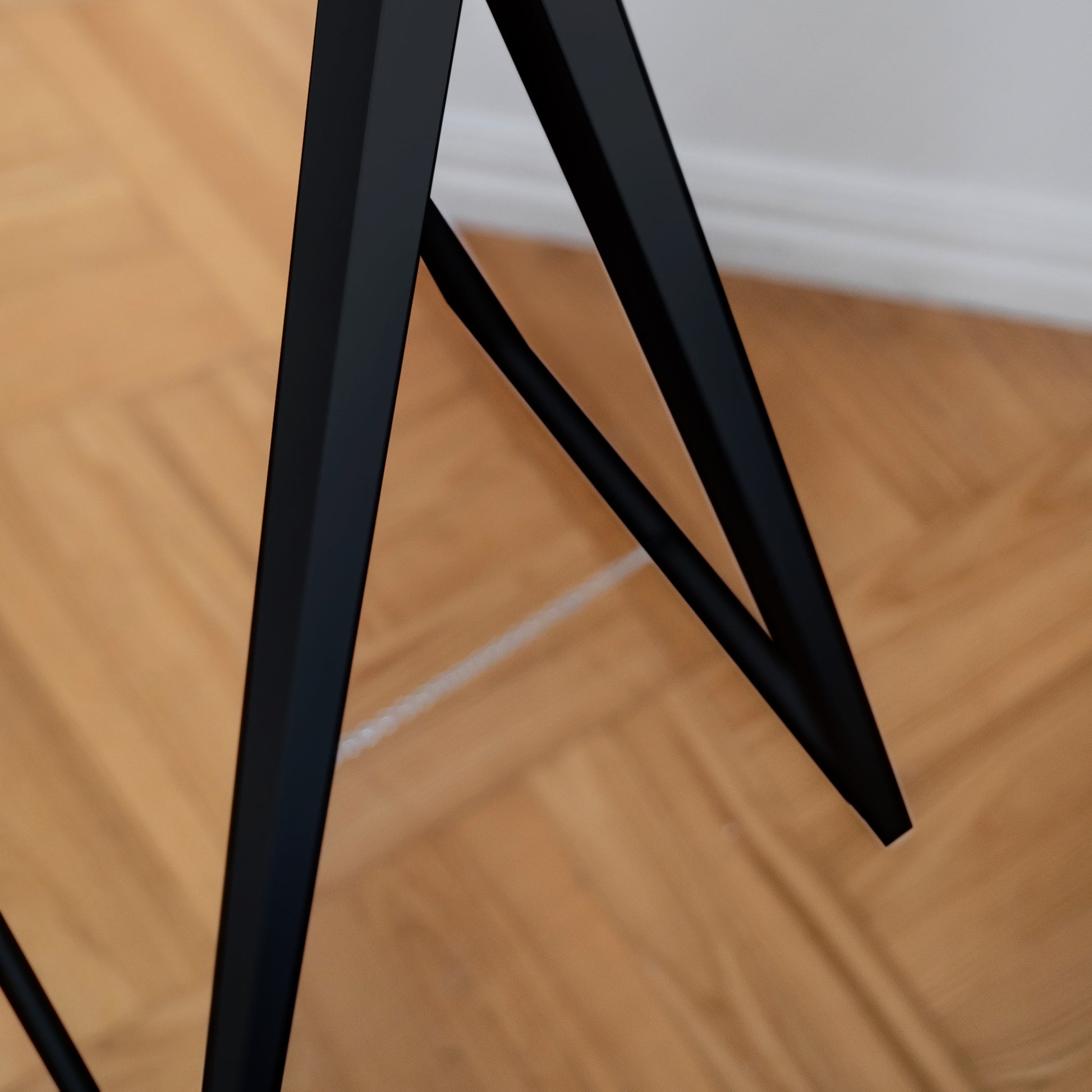 Dolna część stojaka lustra Verona w czarnej ramie na tle drewnianej podłogi.