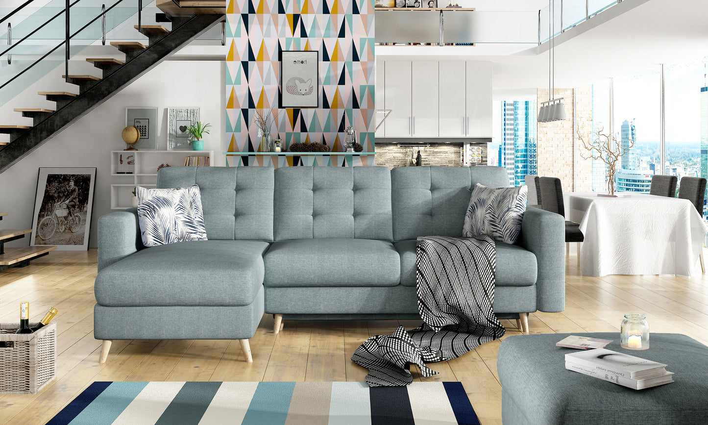 Stylowy narożnik Asgard L w odcieniu delikatnego niebieskiego (Cover 70) z poduszkami Botanical 80, w jasnym, nowoczesnym apartamencie z widokiem na miasto.