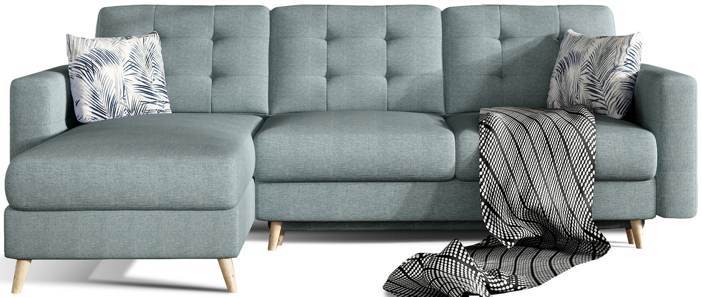 Niebieski narożnik Asgard L w tkaninie Cover 70 z botanicznymi poduszkami w liście (Botanical 80), osadzony na drewnianych nóżkach z geometrycznym pikowaniem.