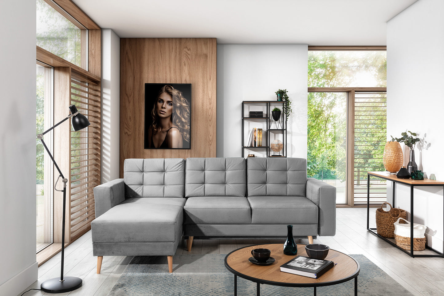 Nowoczesny narożnik Asgard L w tkaninie Monolith 84 jasnoszary w eleganckim salonie z dużymi oknami i drewnianymi akcentami, ustawiony na jasnej podłodze z dywanem.