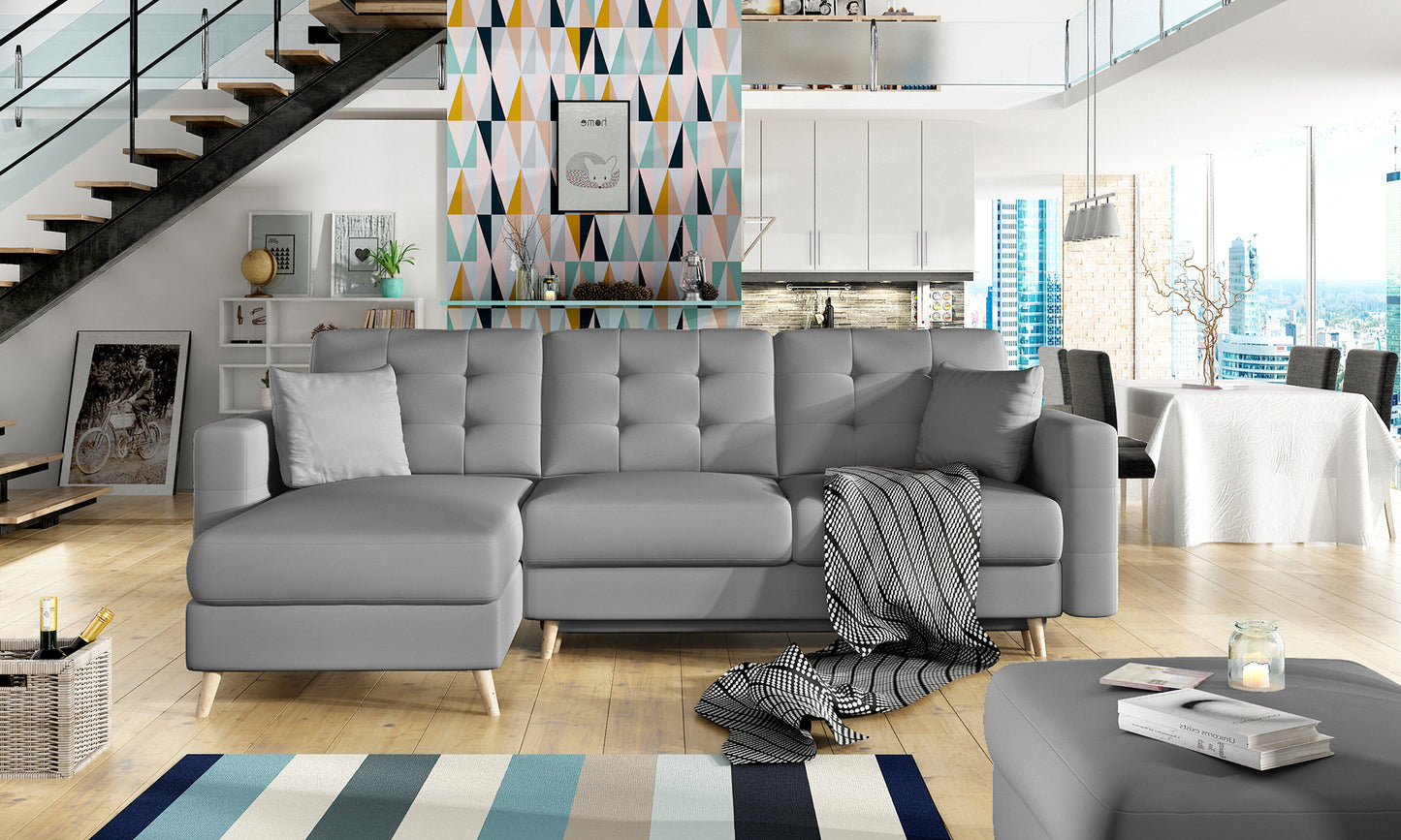 Narożnik Asgard L w tkaninie Soft 29 szary we wnętrzu nowoczesnego salonu z drewnianą podłogą, pastelową tapetą i dużymi oknami z widokiem na miasto.