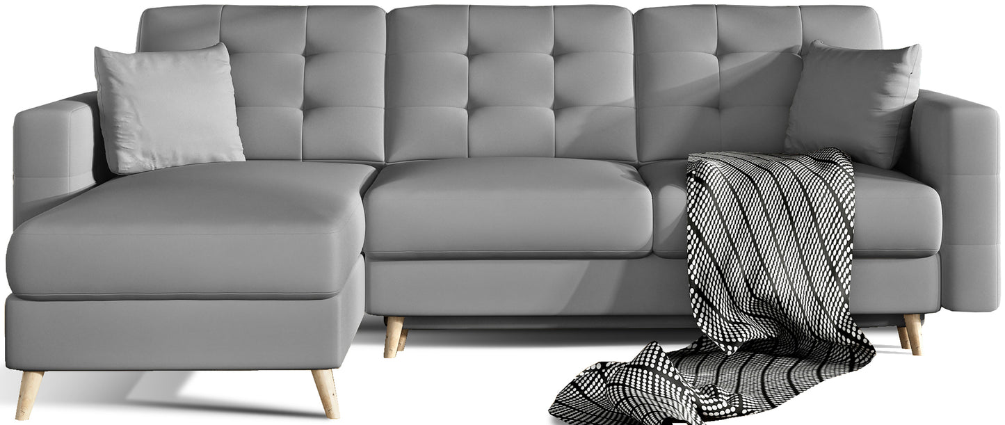 Narożnik Asgard L w kolorze Soft 29 szary, ustawiony na białym tle, prezentujący nowoczesne pikowane oparcie, jasnoszare poduszki i dekoracyjny koc w geometryczny wzór.