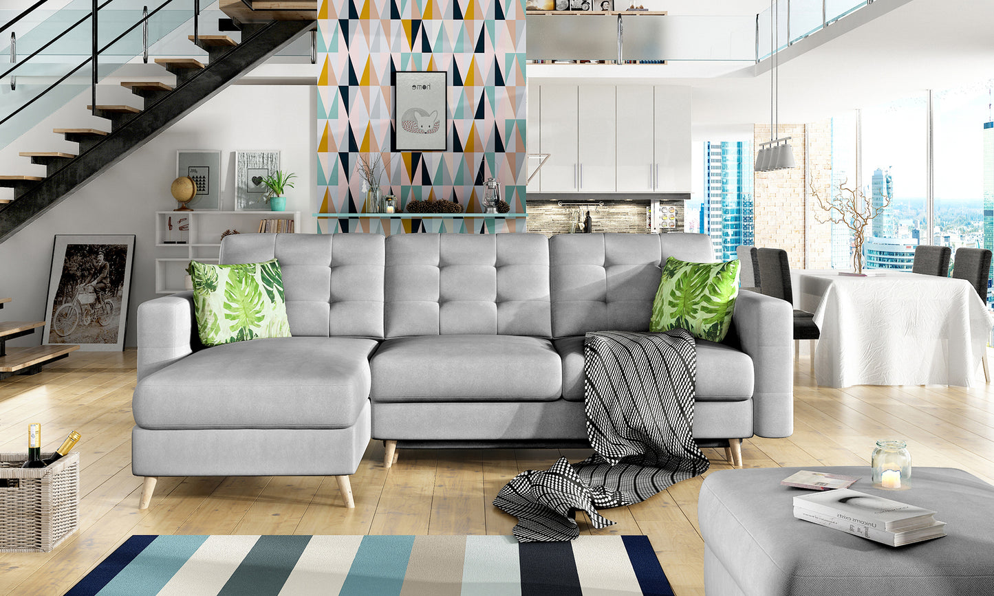 Nowoczesny salon z narożnikiem Asgard L w odcieniu Soro 83 i poduszkami Jungle 32 – jasnoszara sofa w przestrzeni z drewnianą podłogą i geometryczną ścianą dekoracyjną.