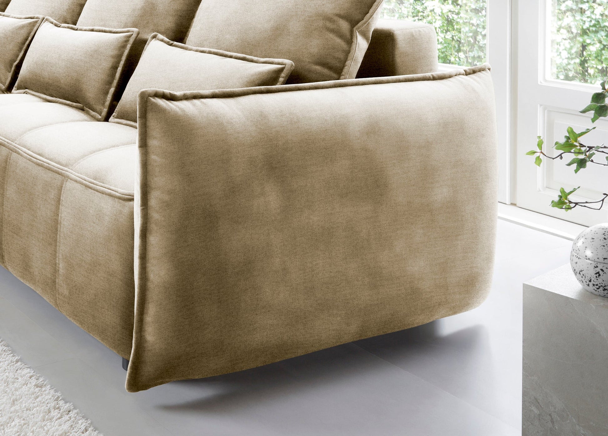 Detal zaokrąglonego podłokietnika i tylnej części narożnika Campo w układzie lewym, tapicerka Nube 20 beżowy na tle okna.