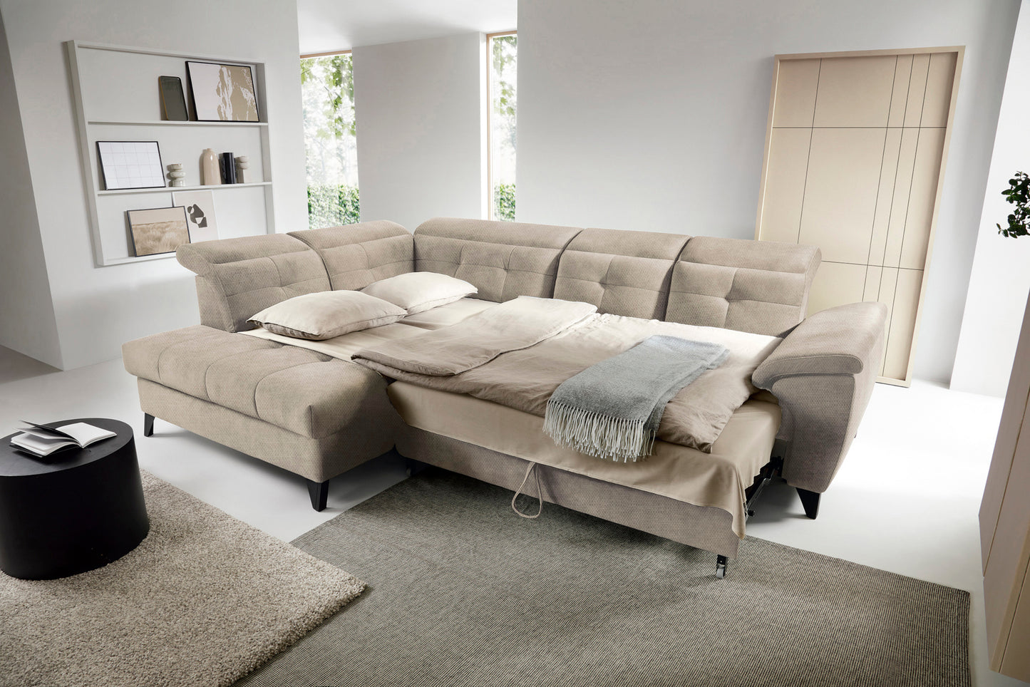 Narożnik Inferne Raquel 20 beżowy w układzie lewym rozłożony jako łóżko, z pościelą i oparciami przestawionymi do spania.