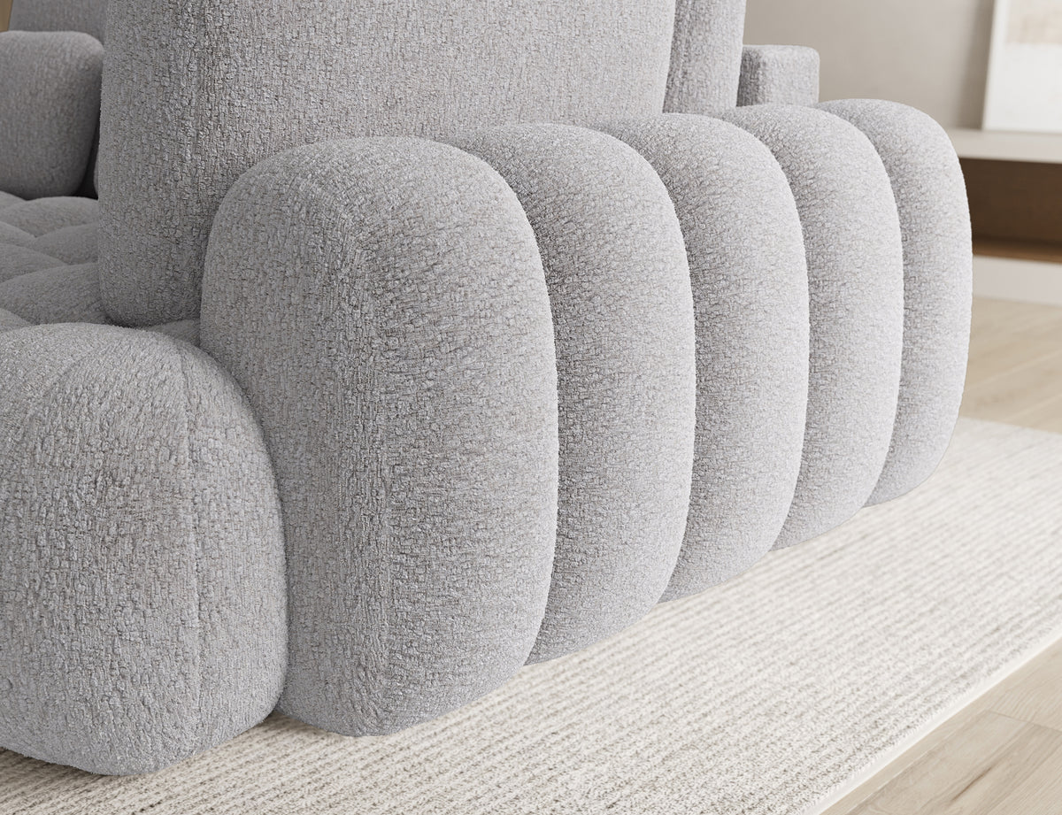 Narożnik Cozion prawy szary, zbliżenie na zaokrąglony podłokietnik i segmentowe elementy bryły pokryte strukturalną tkaniną.