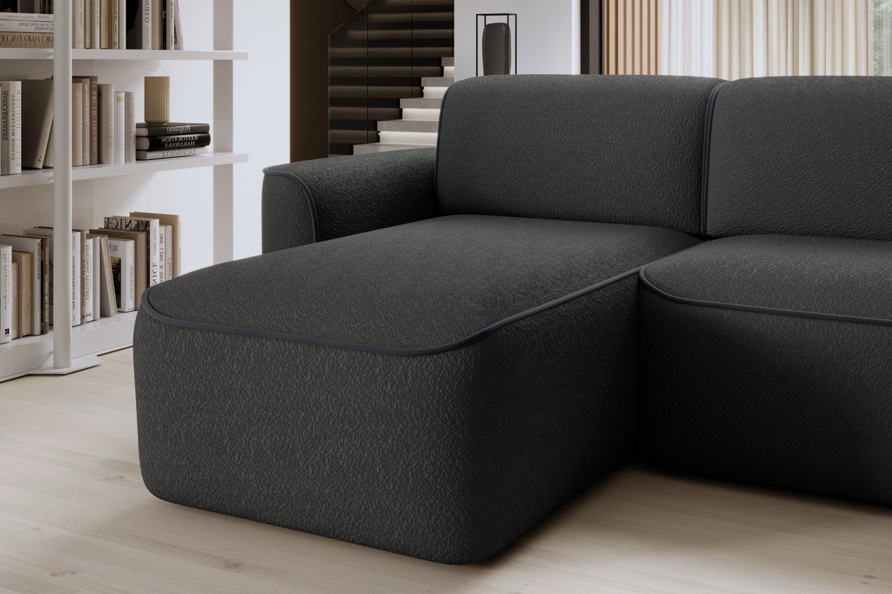 Zbliżenie przedniej krawędzi szezlongu po lewej stronie narożnika Ume, miękka tapicerka Royal 05 czarny obwiedziona dyskretną lamówką w ciemnoszarym kolorze.