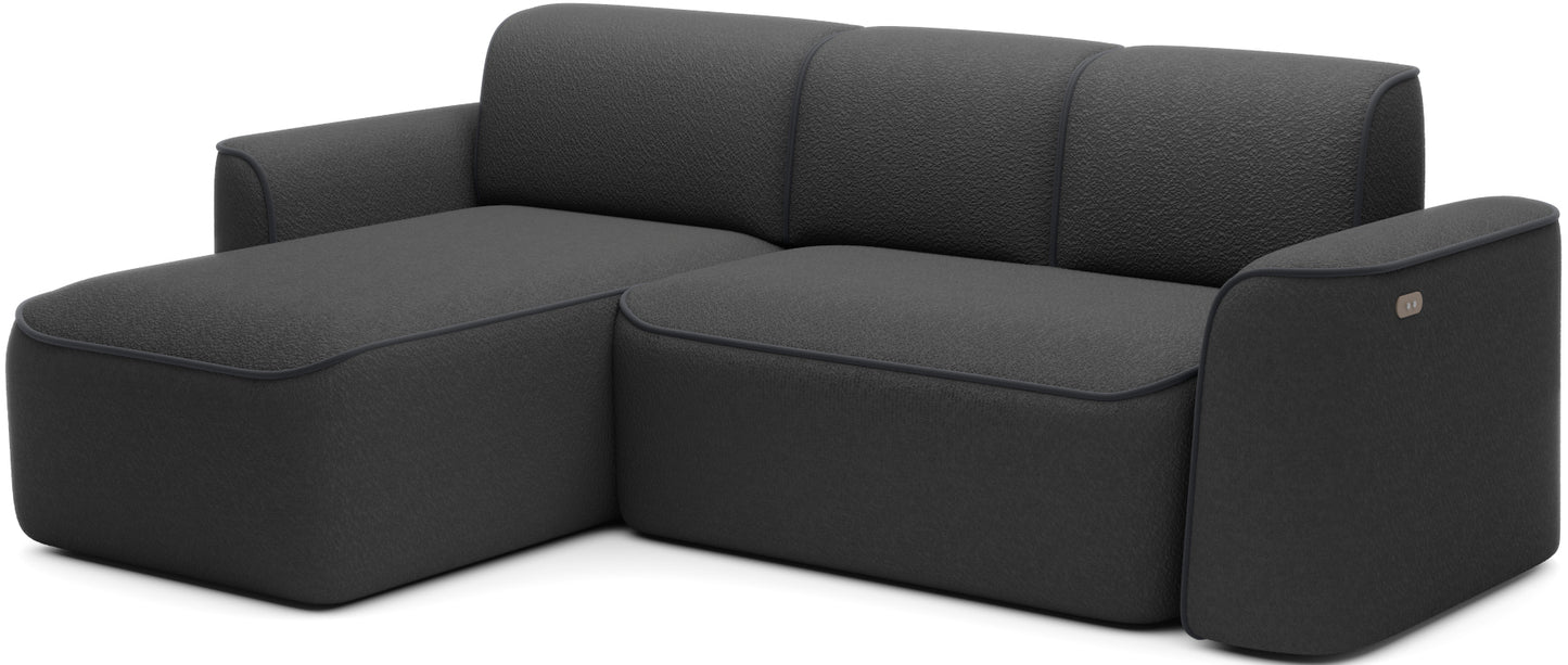 Ukosny widok narożnika Ume w układzie lewym, wyraźnie zaznaczony szezlong po lewej i subtelne lamówki Velvetmat 06 ciemnoszary na czarnym bouclé.