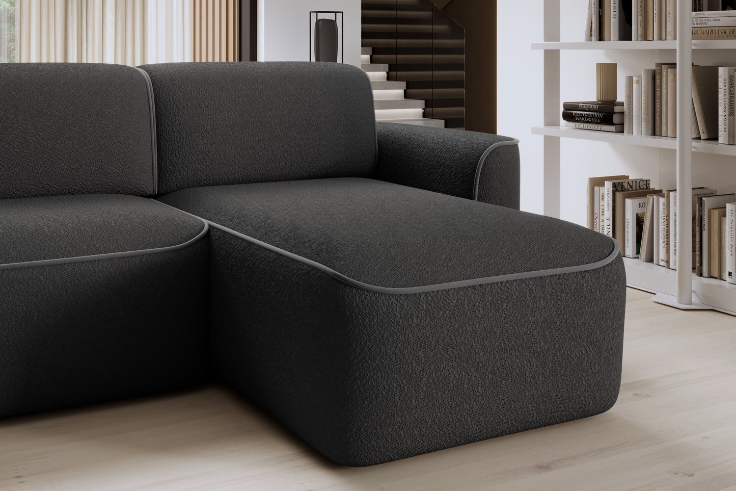 Zbliżenie przedniej krawędzi otomanki narożnika Ume w układzie prawym, czarne bouclé z subtelną szarą lamówką.