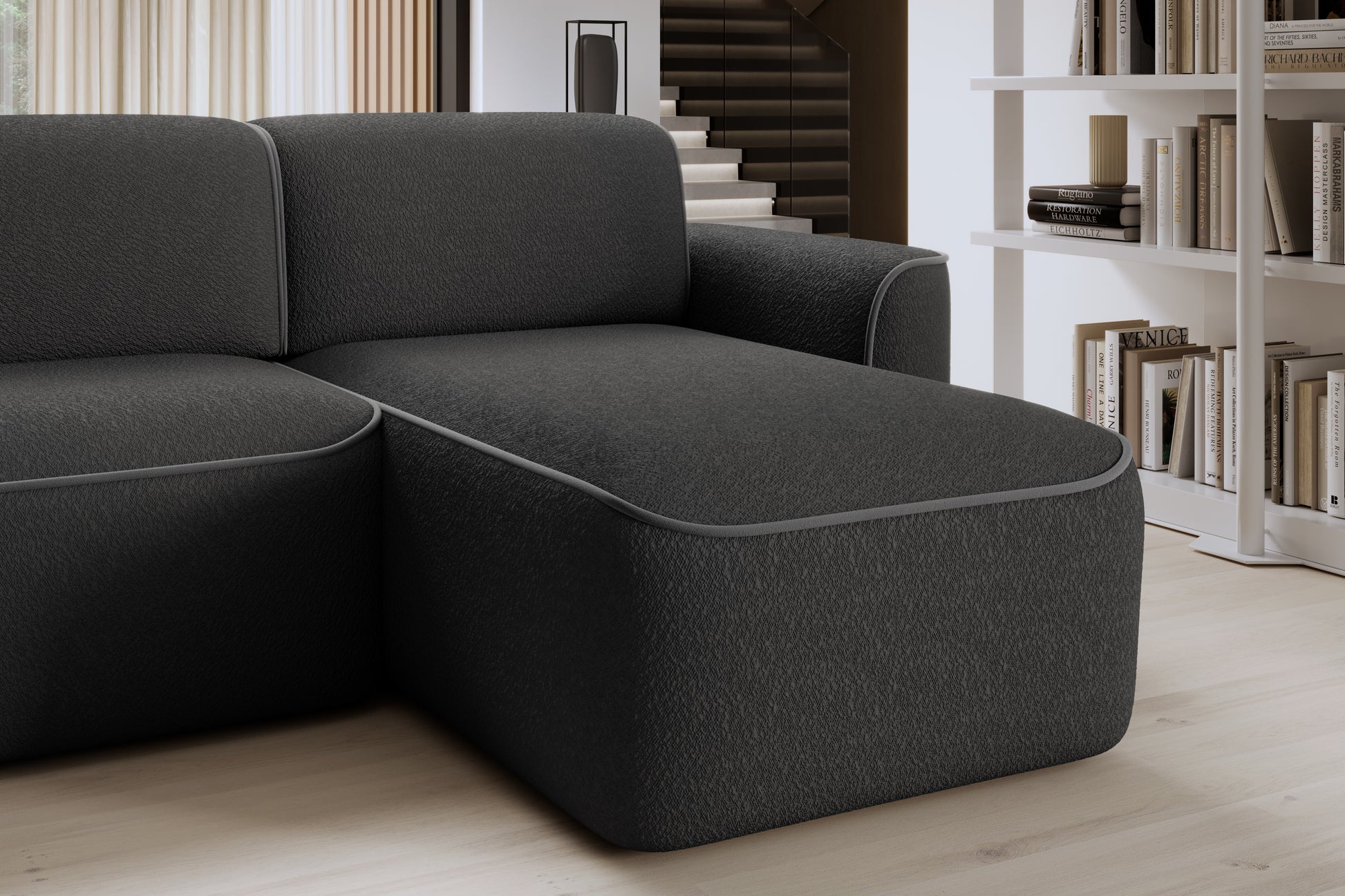 Zbliżenie przedniej krawędzi otomanki narożnika Ume w układzie prawym, czarne bouclé z subtelną szarą lamówką.