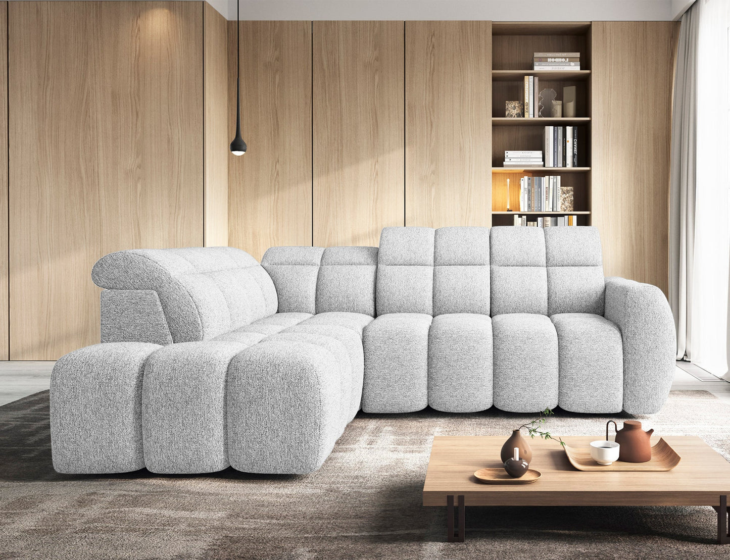 Narożnik Falconn lewostronny Coralline 01 w jasnym salonie, ustawiony na tle drewnianej zabudowy z regałem, przy niskim stoliku kawowym.