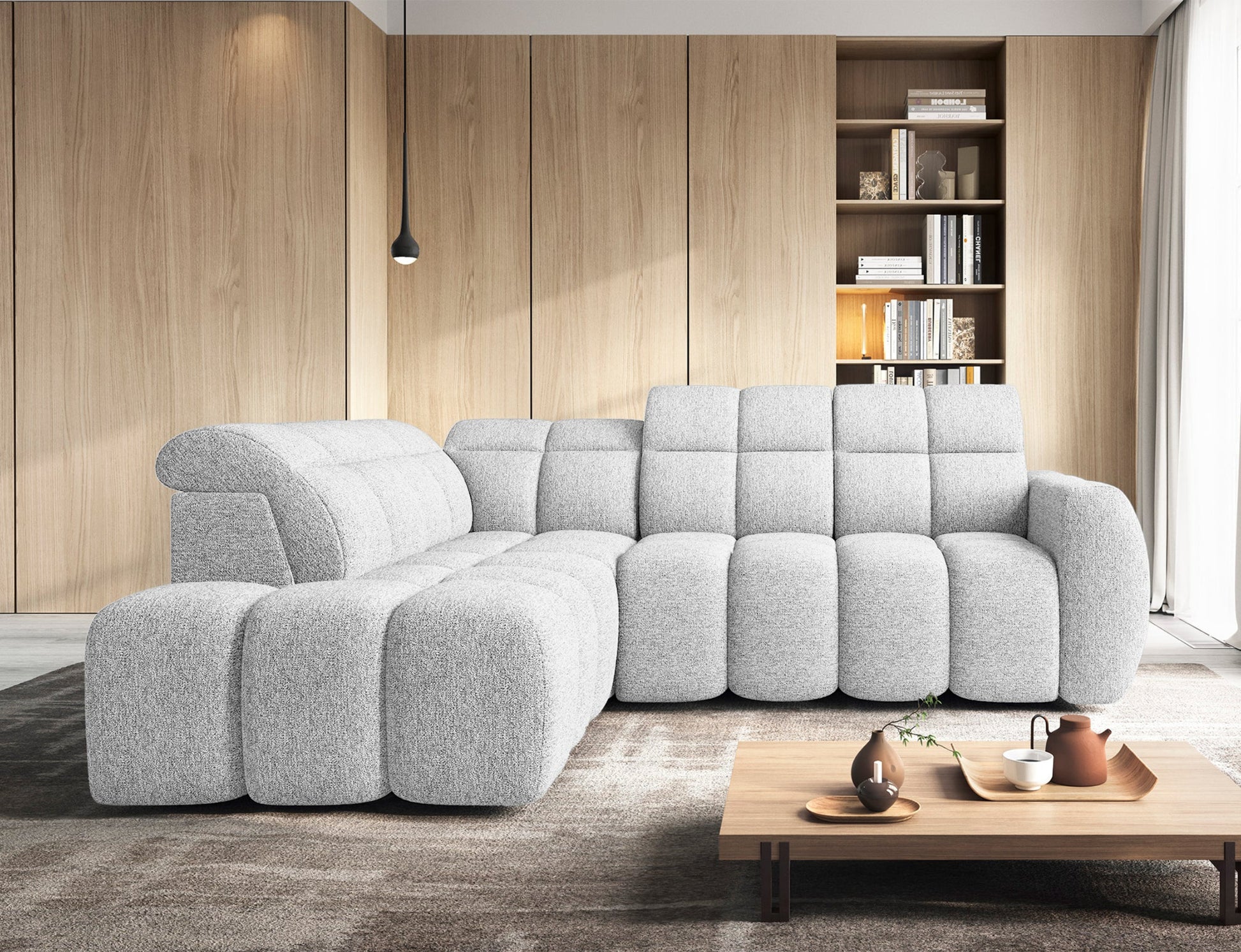 Narożnik Falconn lewostronny Coralline 01 w jasnym salonie, ustawiony na tle drewnianej zabudowy z regałem, przy niskim stoliku kawowym.