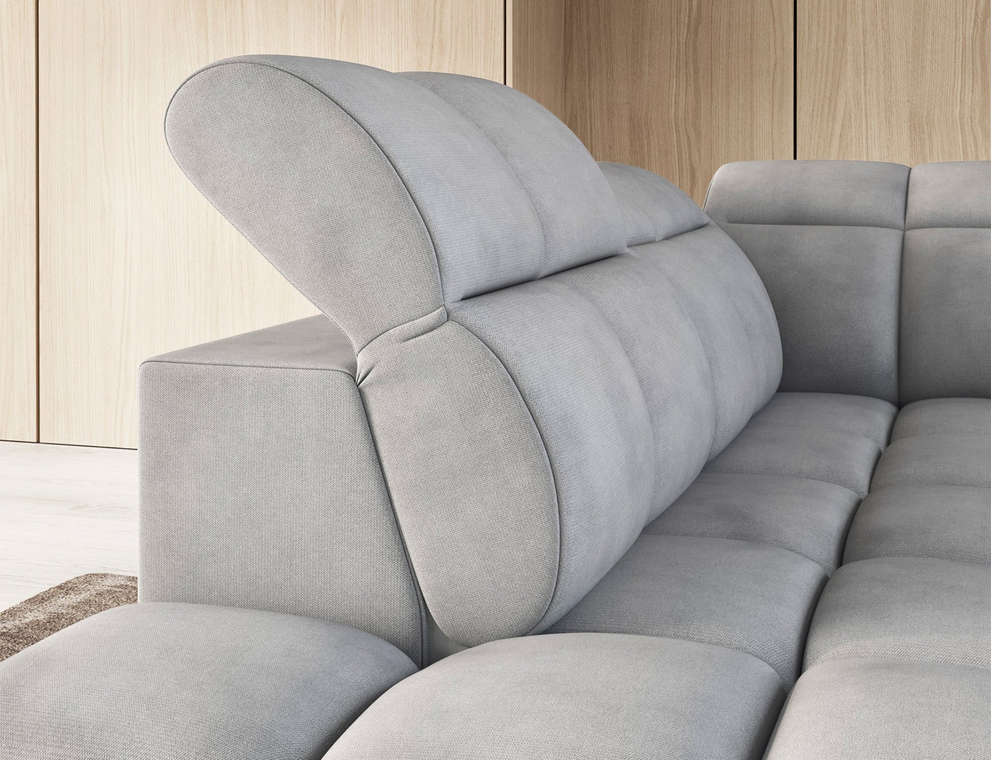 Jasnoszary narożnik Falconn Sola 04 z podniesionym zagłówkiem i pikowanym oparciem, w nowoczesnym wnętrzu z drewnianymi panelami ściennymi.