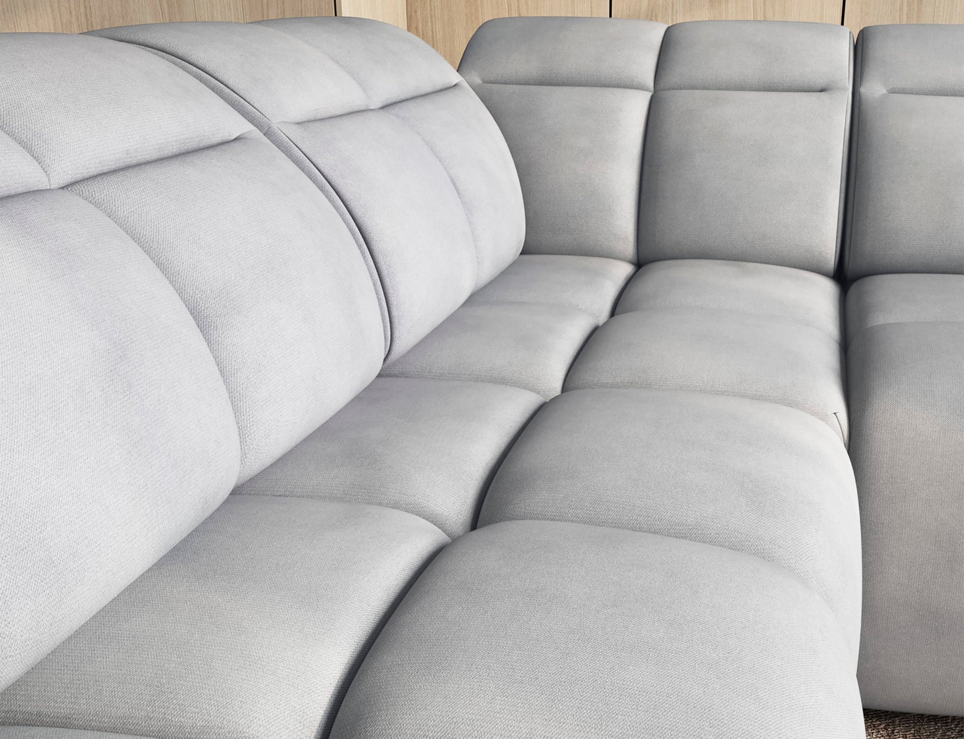 Narożnik Falconn Sola 04 w jasnoszarym kolorze z miękką tapicerką i pikowanymi siedziskami w nowoczesnym wnętrzu z drewnianą zabudową.