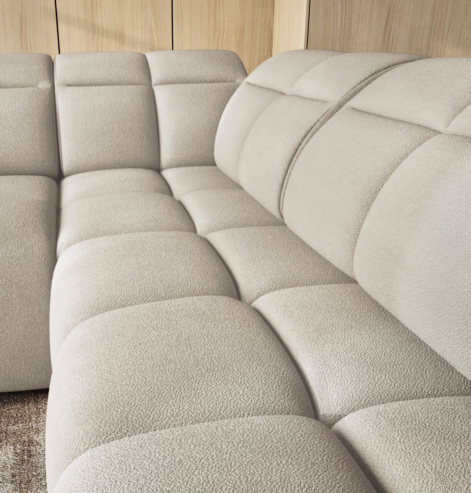 Zbliżenie na głęboko pikowane siedzisko narożnika Falconn Royal-18, tapicerowanego jasną, przytulną tkaniną bouclé.