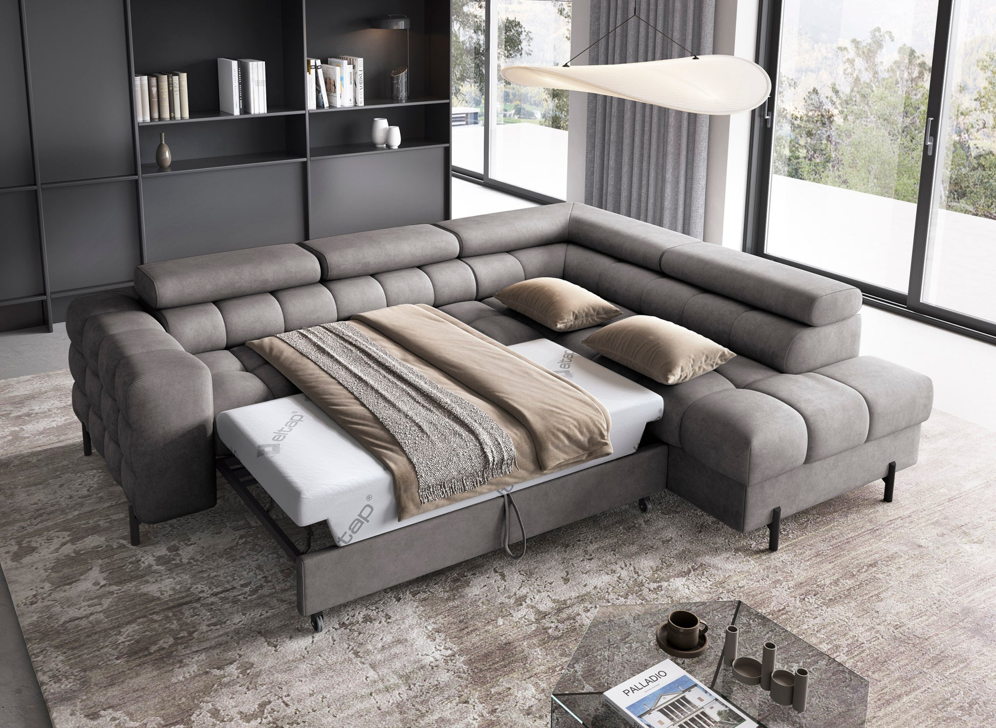Rozłożony narożnik Ferucce w tkaninie Aura 04 szary, z funkcją spania i pościelą, ustawiony w nowoczesnym, jasnym salonie z dużymi oknami.