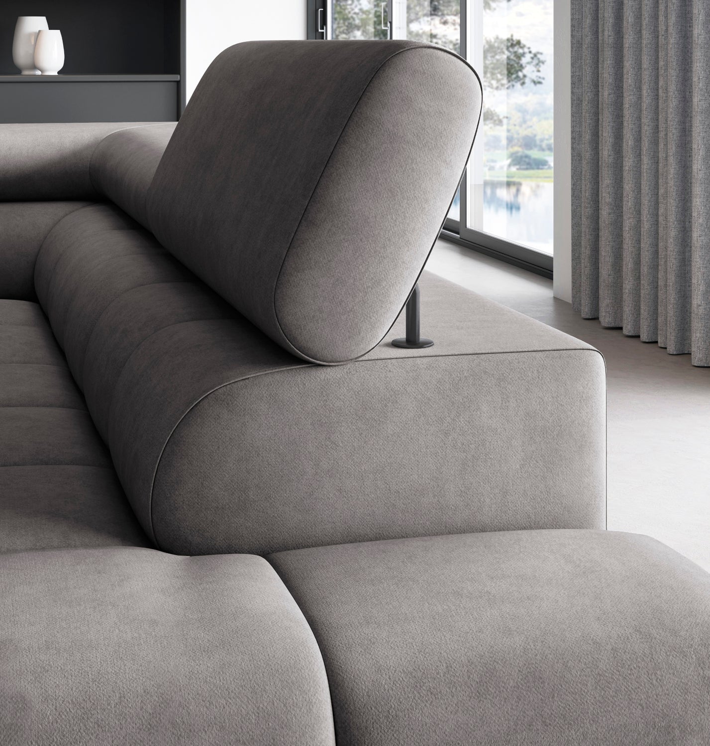 Zbliżenie na regulowany zagłówek narożnika Ferucce w tkaninie Aura 04 szary, z widocznym boczkiem i przeszyciami siedziska, na tle przeszklonych drzwi balkonowych i zasłon.