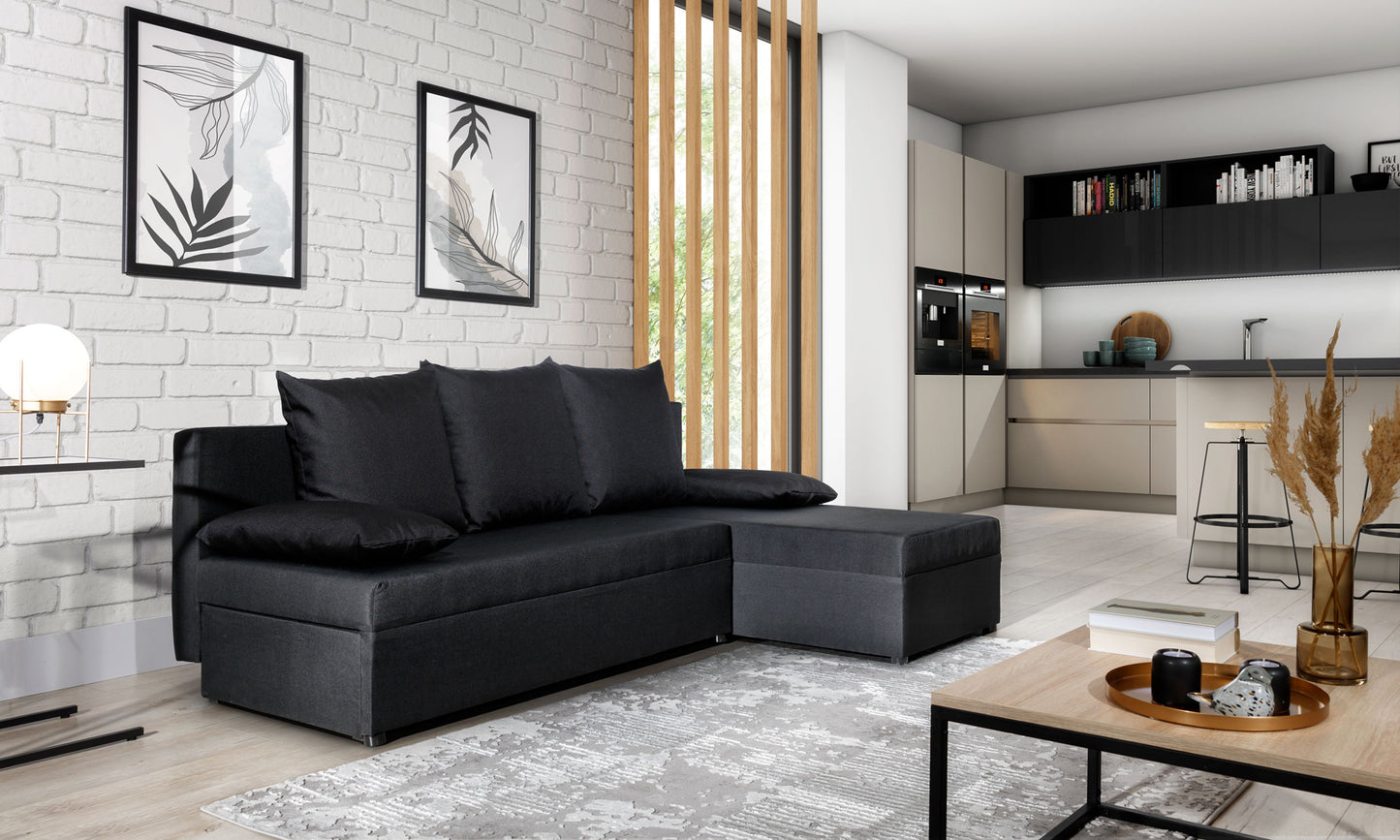 Narożnik Gino w kolorze Sawana 14 czarny, ustawiony w nowoczesnym salonie z białą ceglaną ścianą i jasną kuchnią w tle.