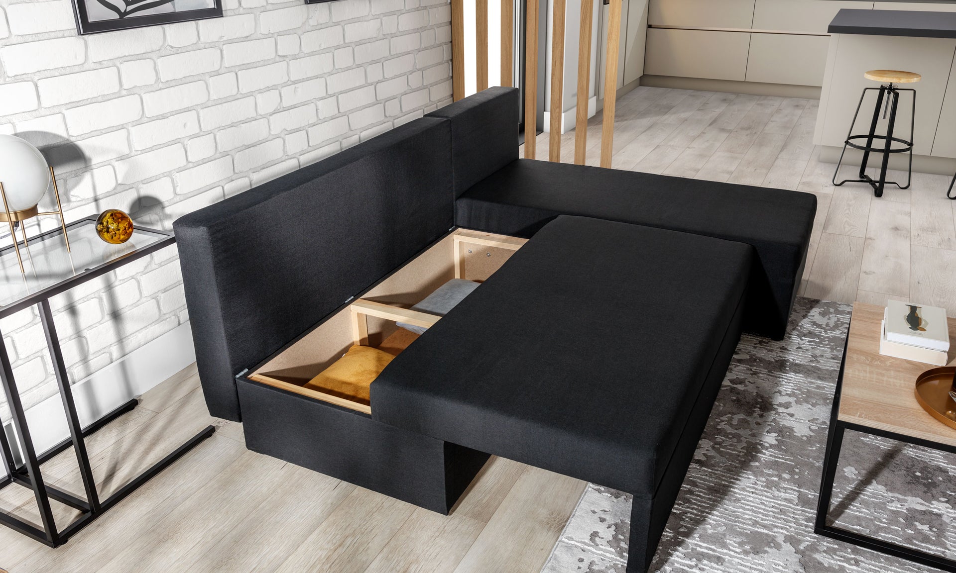 Narożnik Gino w kolorze Sawana 14 czarny z otwartym pojemnikiem na pościel, w aranżacji jasnego salonu.