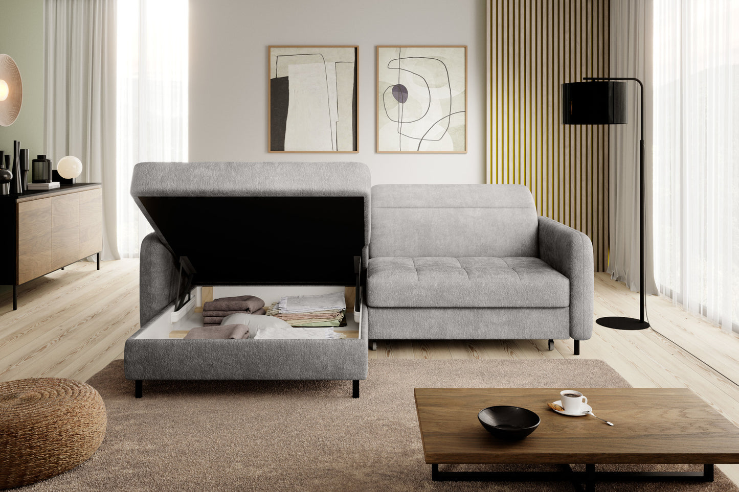 Narożnik Gomsi Raquel 03 jasnoszary w układzie lewym z uniesionym siedziskiem odsłaniającym pojemny schowek, w przytulnym salonie z dywanem i dekoracją ścienną.