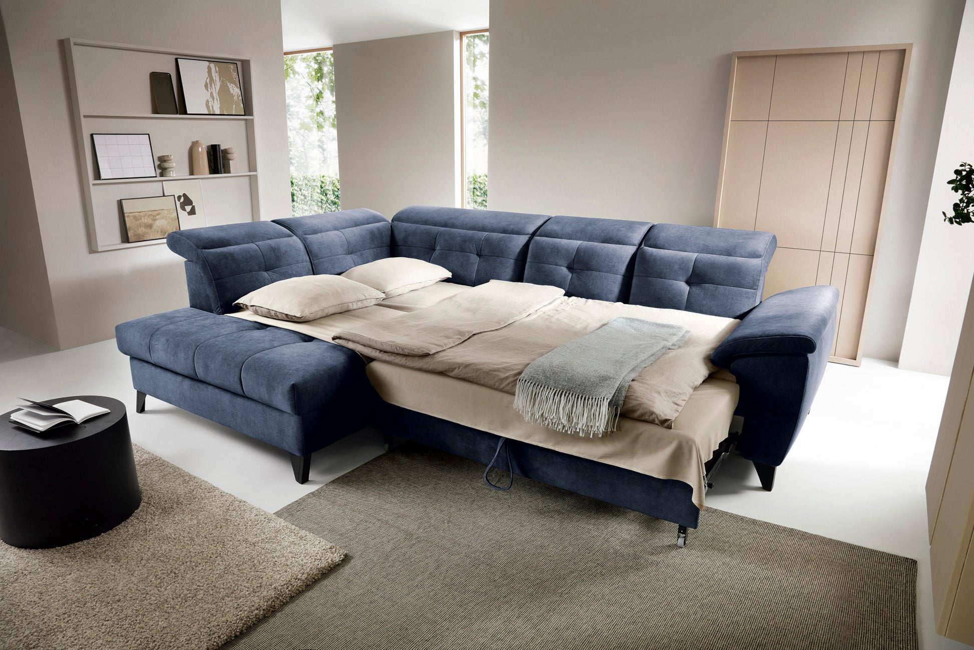 Narożnik Relax 40 grafitowy w układzie lewym rozłożony jako łóżko z pościelą, w tle stylowy dywan i minimalistyczne dekoracje ścienne.