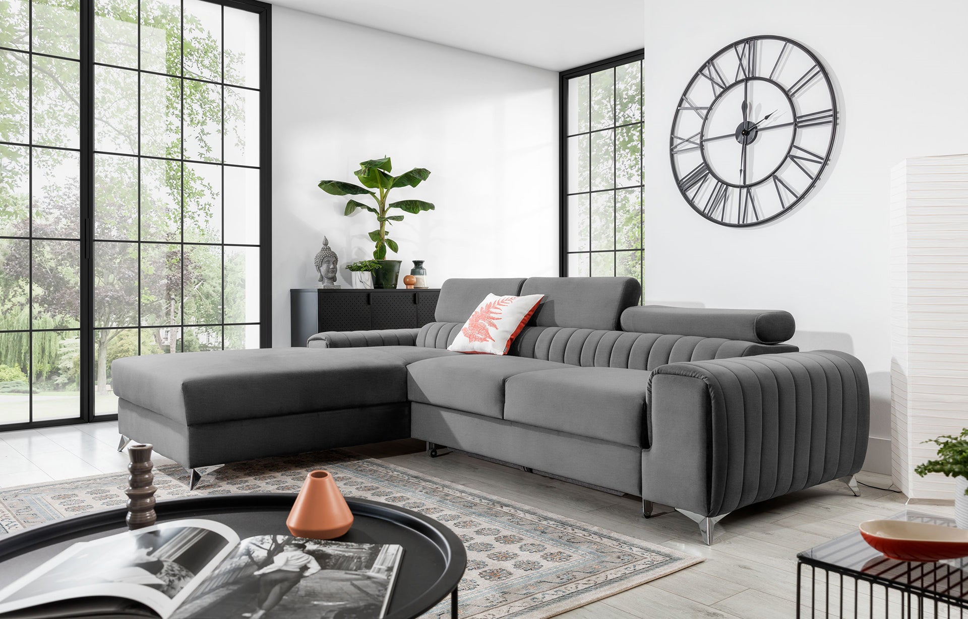 Narożnik Grayson Nube 03 jasnoszary w aranżacji salonu z dużymi oknami, dekoracyjną poduszką i roślinami w tle.