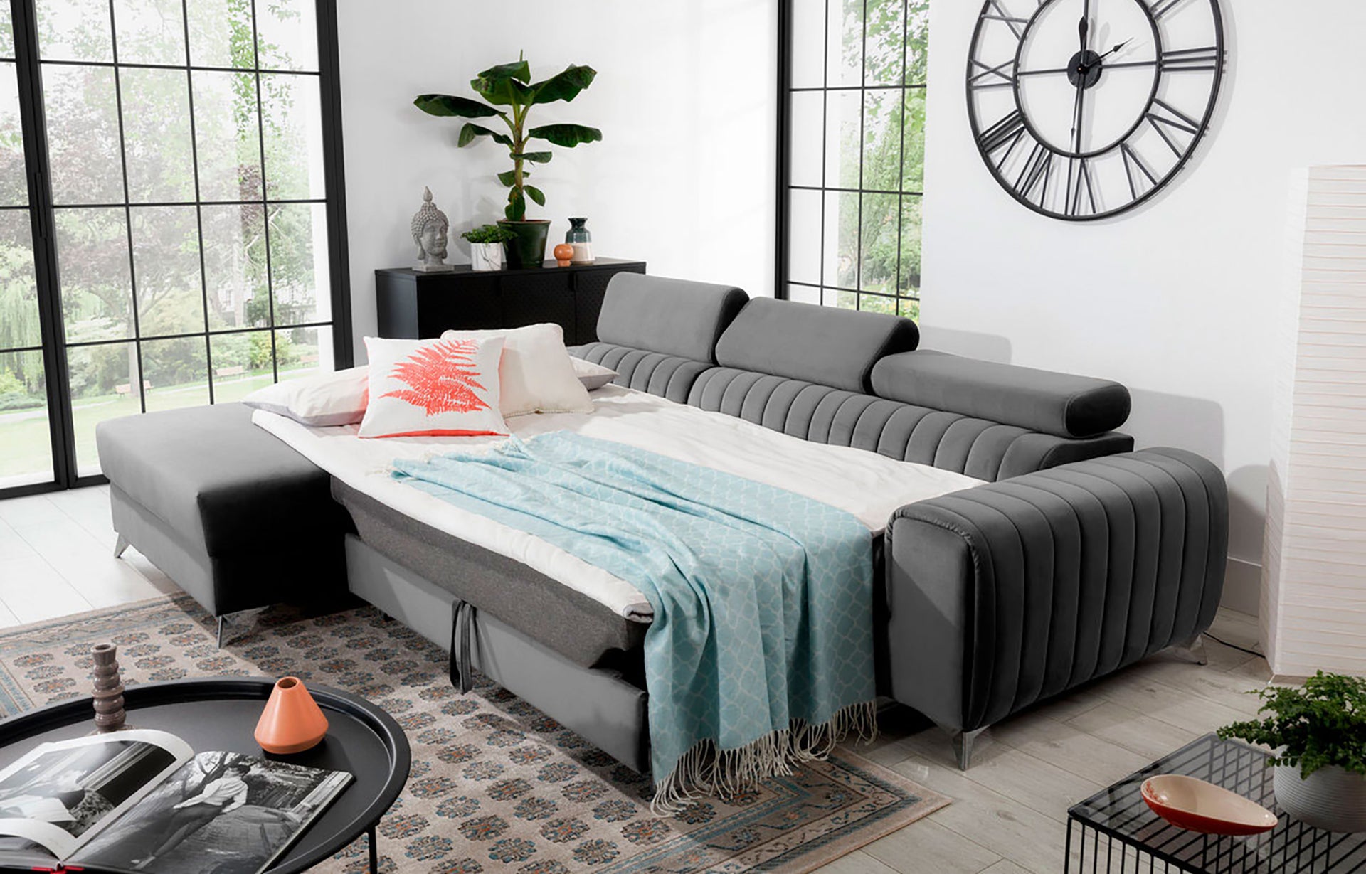 Narożnik Grayson jasnoszary rozłożony do funkcji spania – komfortowe łóżko z pościelą i kocem w aranżacji wnętrza.