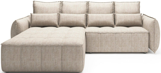 Frontowy widok narożnika Campo w układzie lewym obitego tkaniną Manhattan 18 jasnobeżowy, z szerokim pikowanym szezlongiem po lewej i modułem siedzącym po prawej.