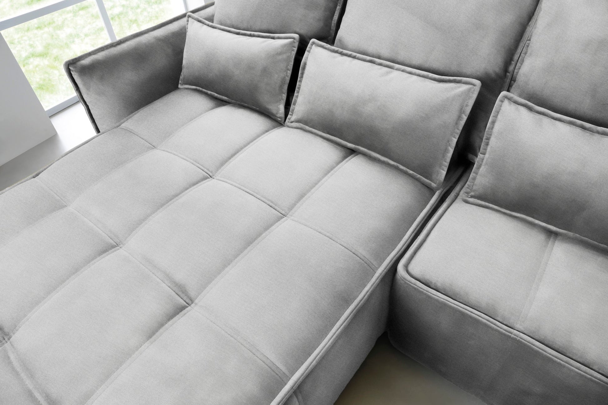 Zbliżenie na pikowane siedzisko i prostokątne poduszki narożnika Campo w układzie lewym, tkanina Nube 03 jasnoszara.