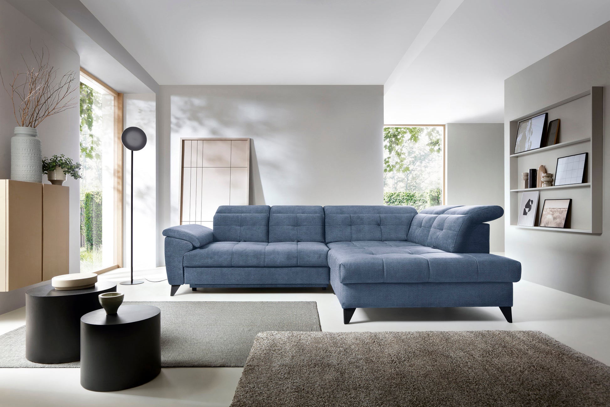 Narożnik Inferne Raquel 40 niebieski w układzie prawym w nowoczesnym salonie obok stojącej lampy i czarnych stolików kawowych.