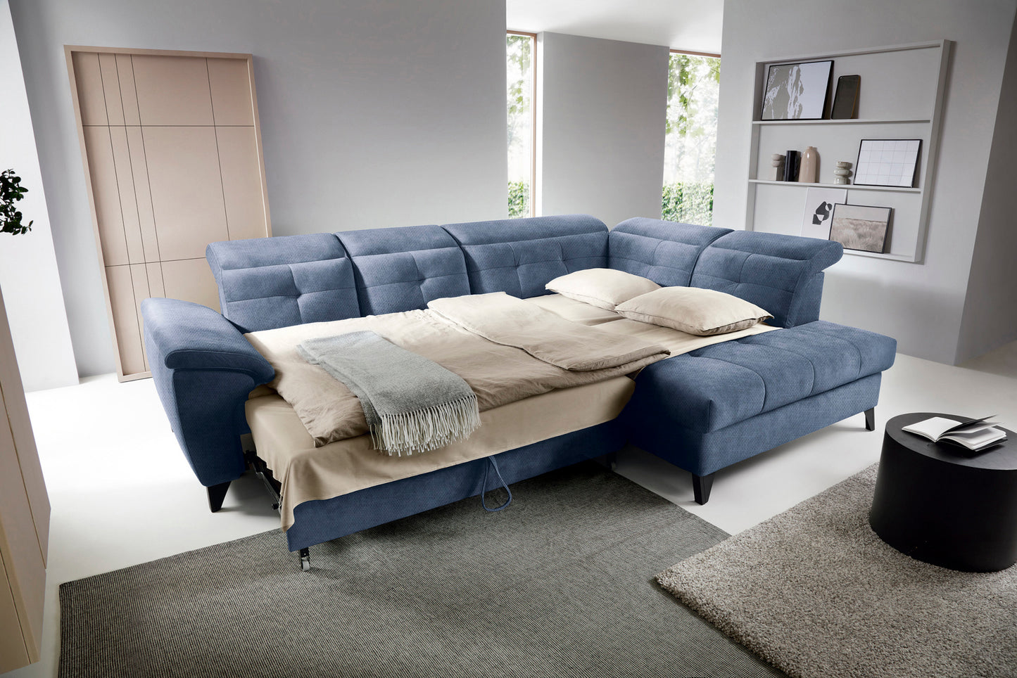 Narożnik Inferne Raquel 40 niebieski w układzie prawym rozłożony jako łóżko, z pościelą i przestawionymi oparciami.