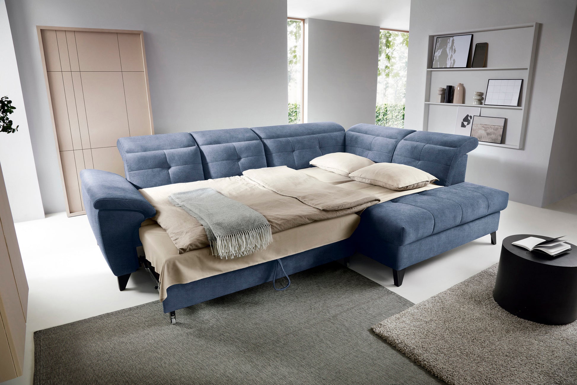 Narożnik Inferne Raquel 40 niebieski w układzie prawym rozłożony jako łóżko, z pościelą i przestawionymi oparciami.