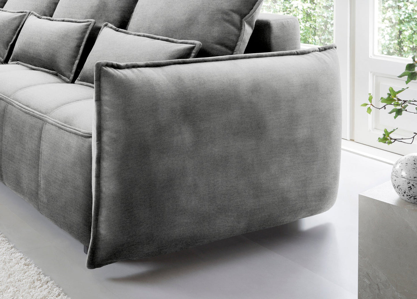 Detal zaokrąglonego podłokietnika i tylnej części narożnika Campo w układzie lewym, tapicerka Nube 04 szary na tle okna.