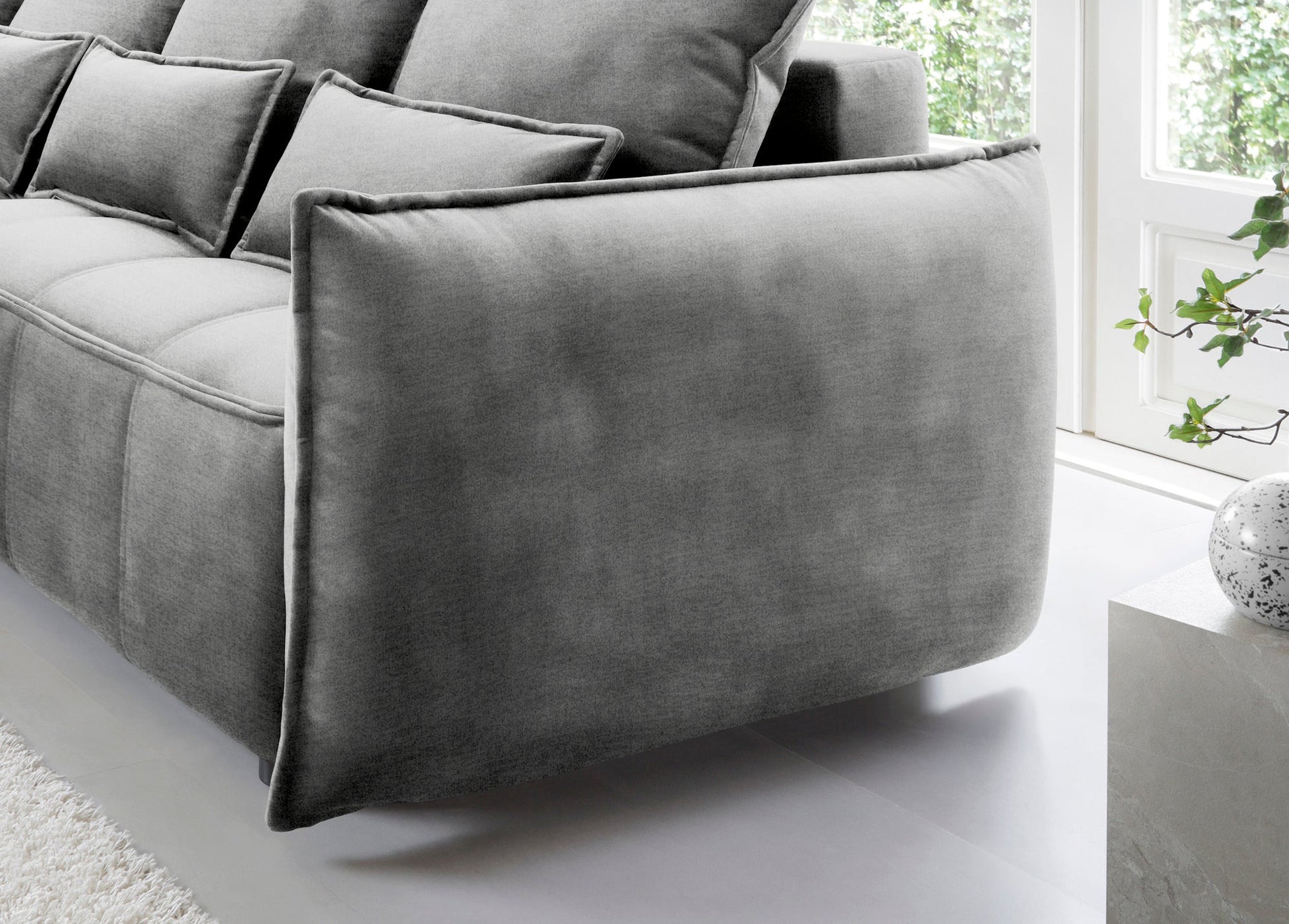 Detal zaokrąglonego podłokietnika i tylnej części narożnika Campo w układzie lewym, tapicerka Nube 04 szary na tle okna.